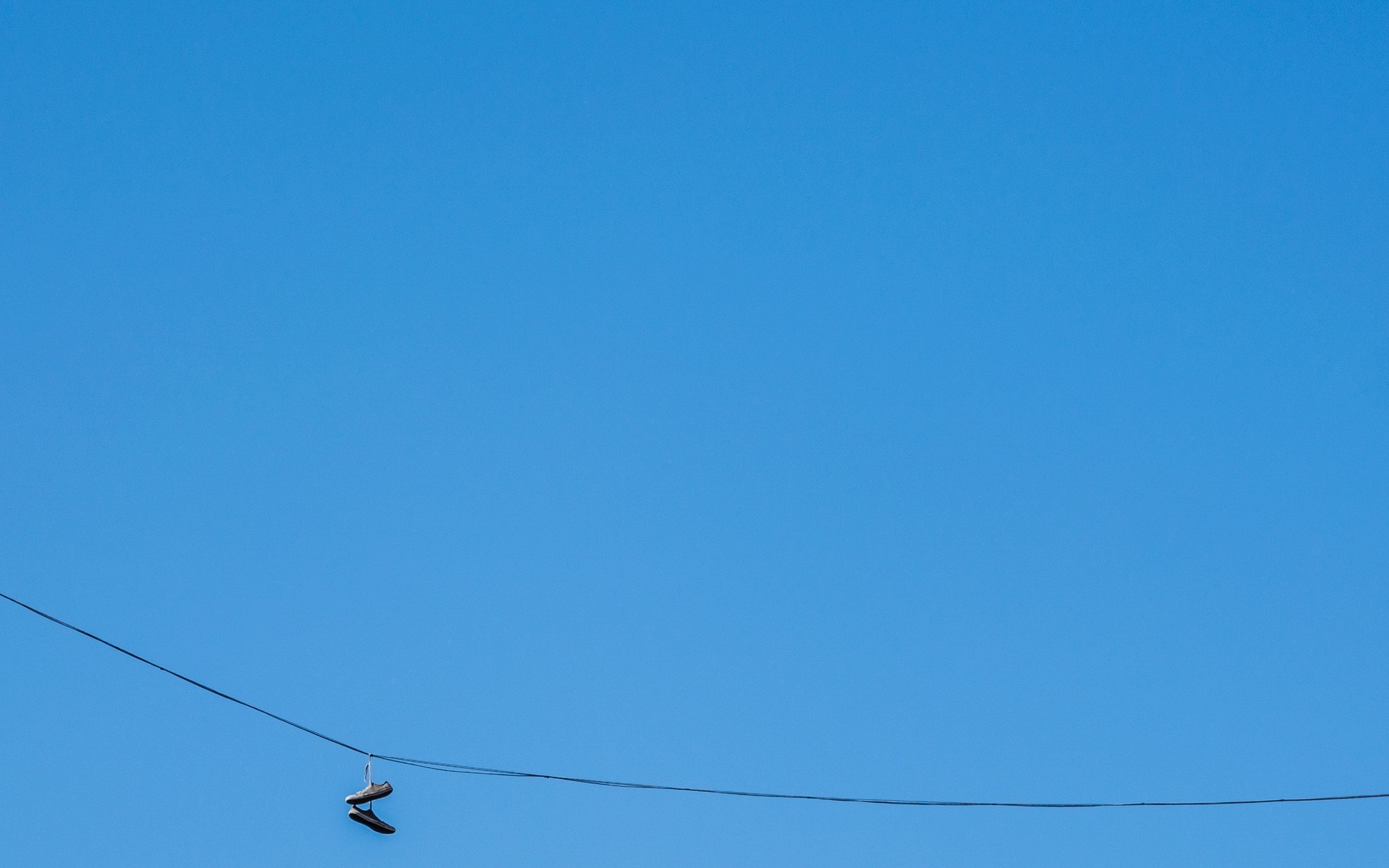 Pair of shoes hanging on a wire against a clear blue sky HD Wallpaper
