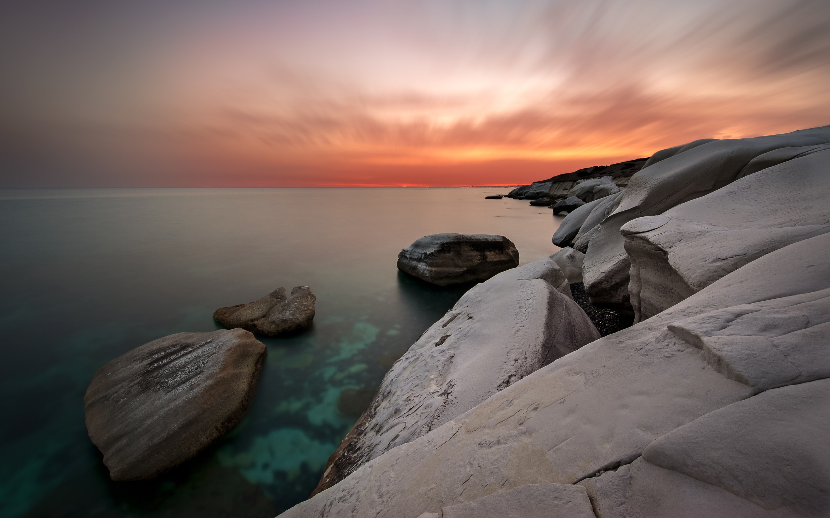 Sunset over rocky coastline with calm sea HD Wallpaper