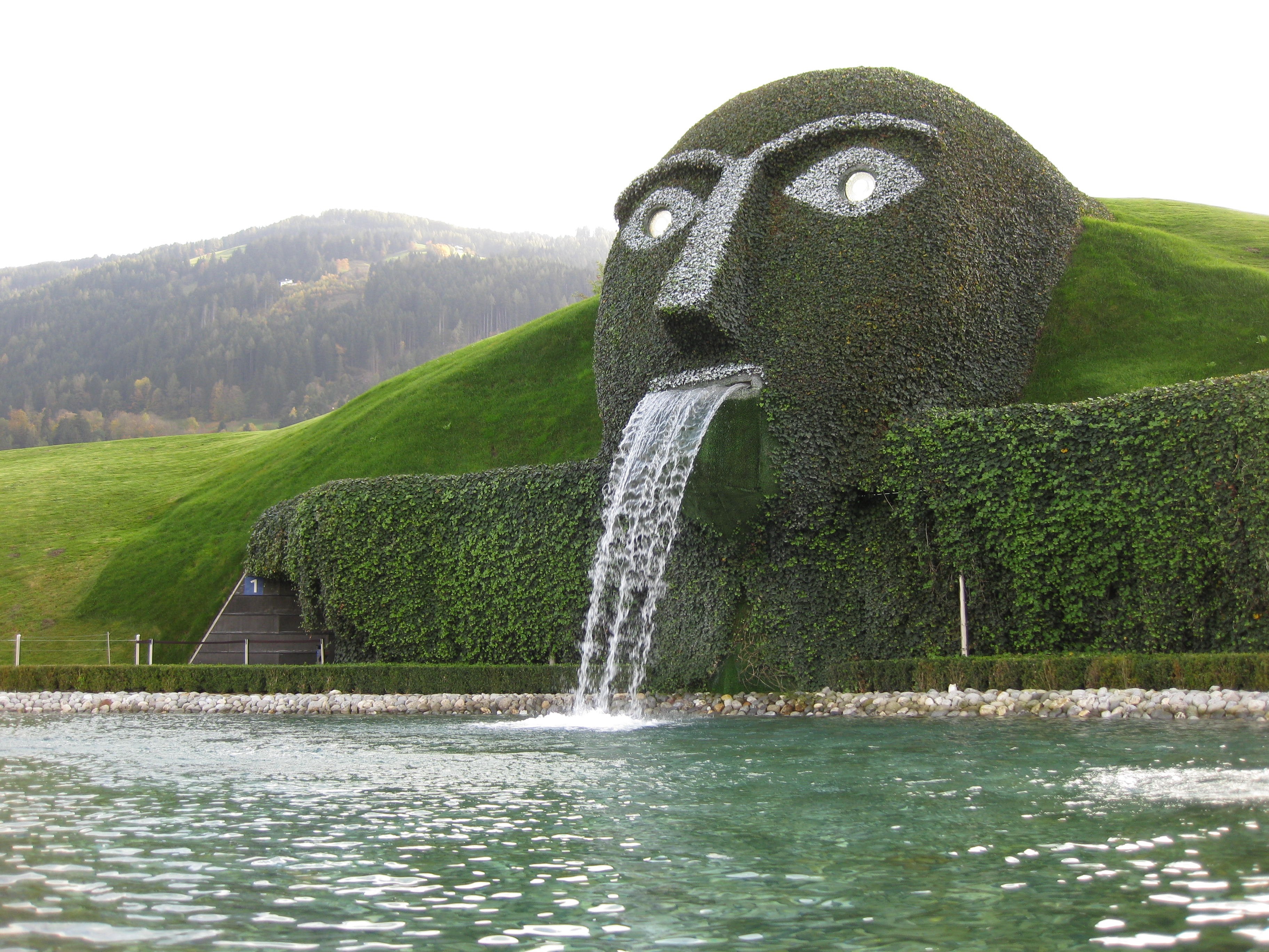 Giant head fountain with water flowing into a pond HD Wallpaper