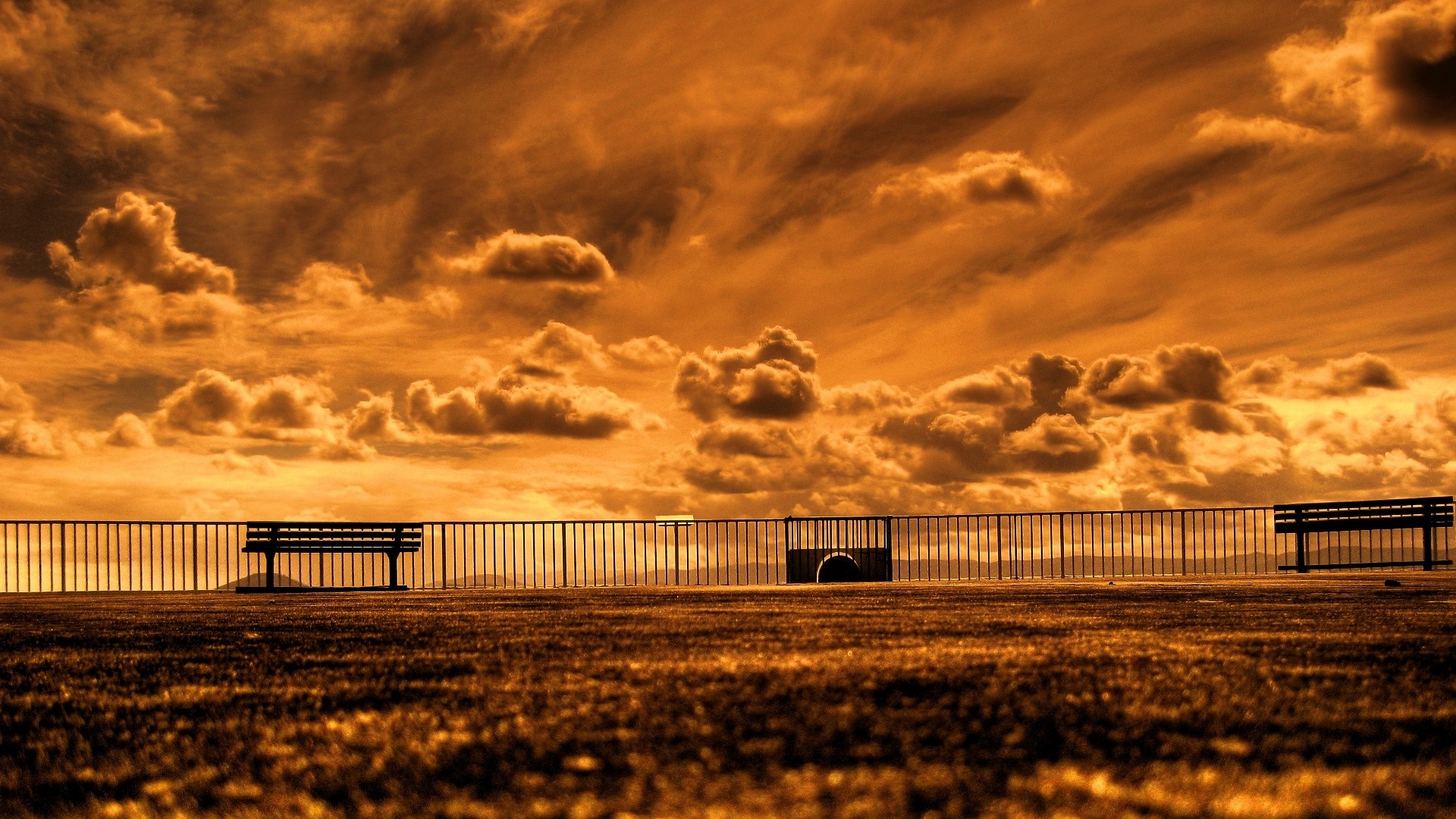 Sepia toned sky with clouds over a fence and benches HD Wallpaper