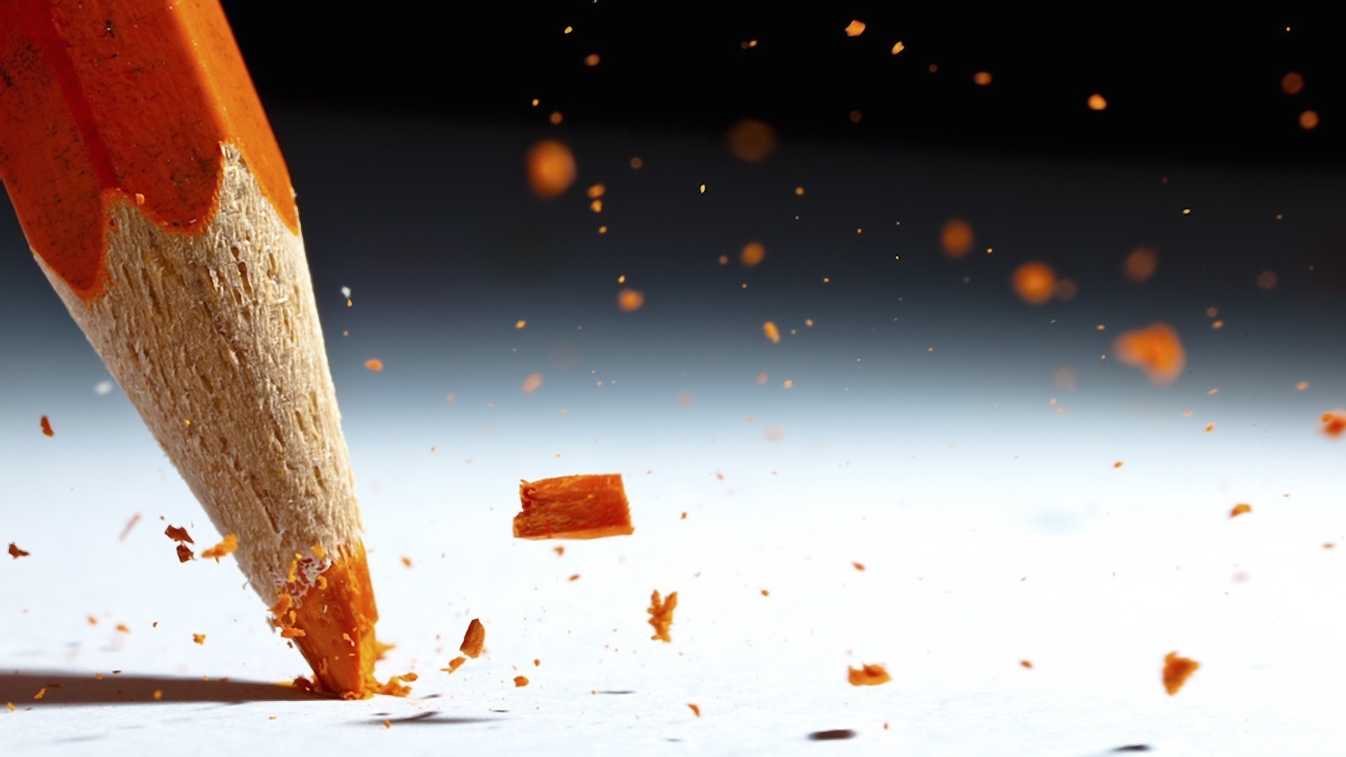 Close-up of an orange pencil breaking, scattering shavings HD Wallpaper