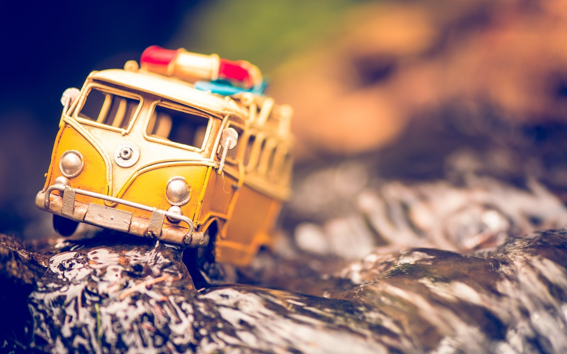Yellow toy bus with red and blue lights on rocks in water HD Wallpaper