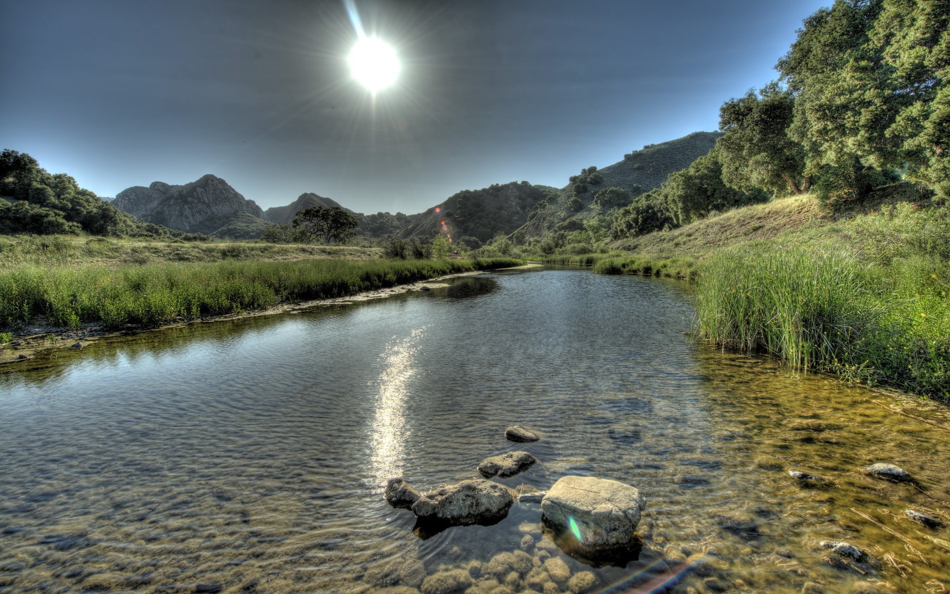 River flowing through a grassy landscape with mountains HD Wallpaper