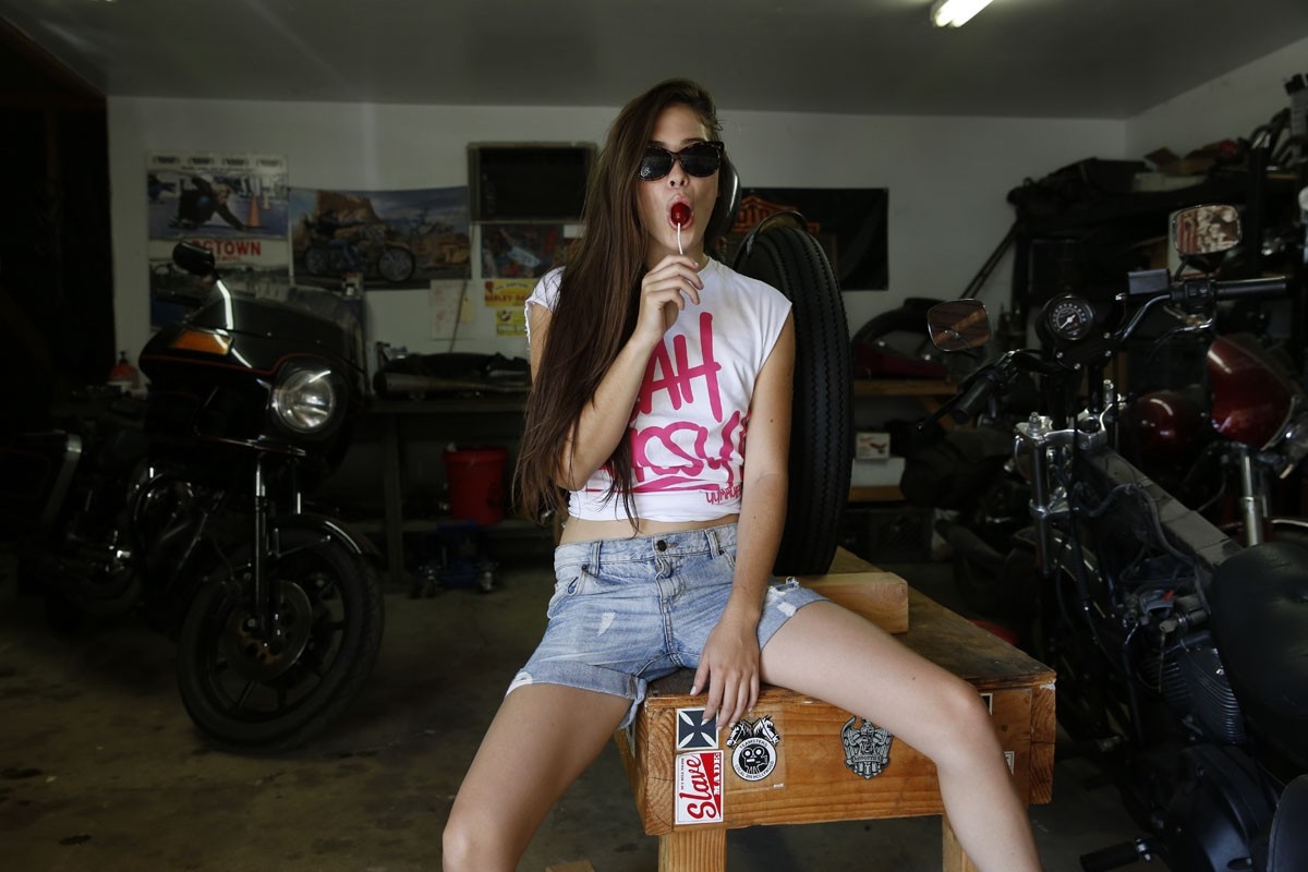 Woman in sunglasses with lollipop in garage with motorcycles HD Wallpaper