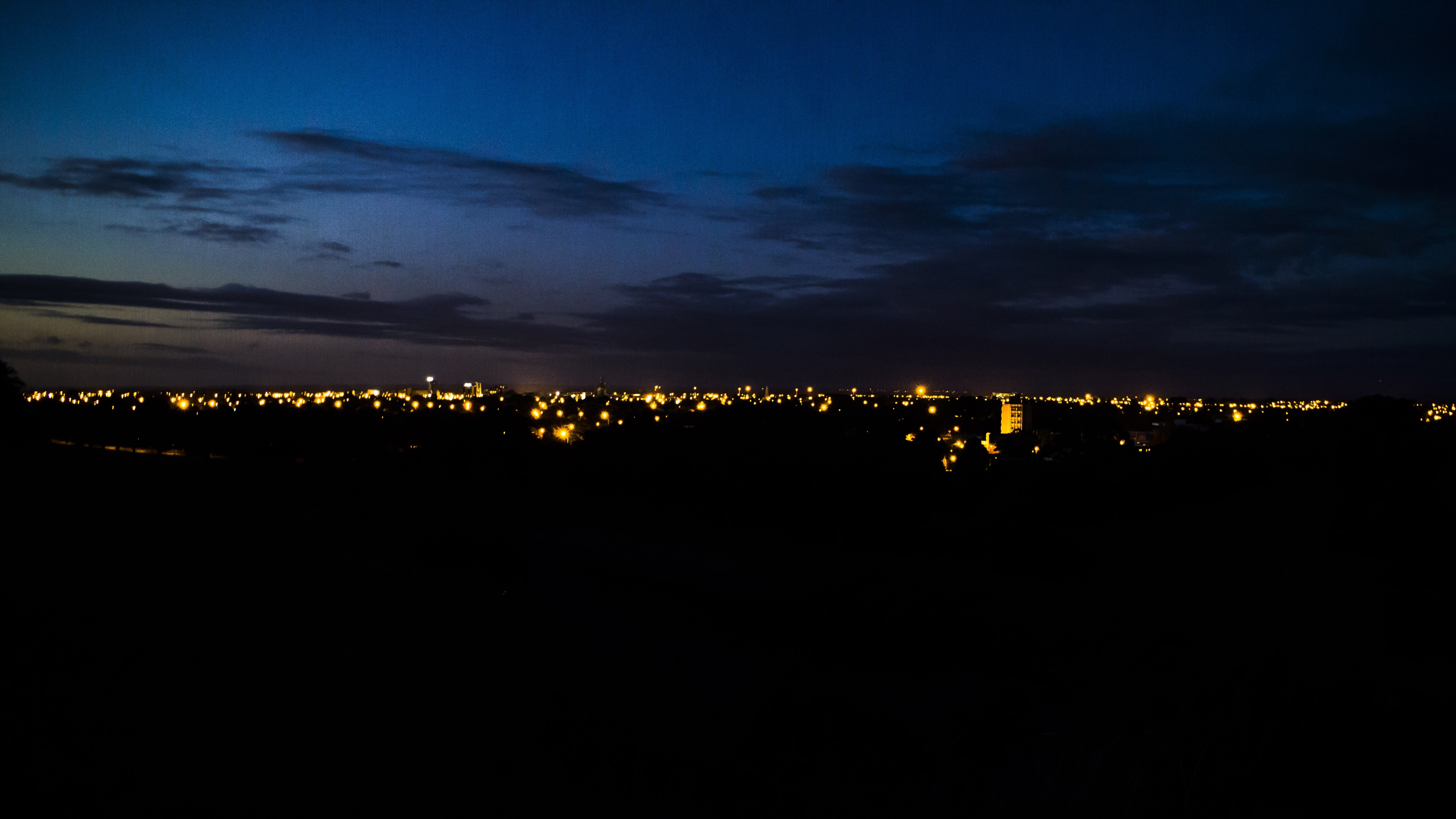 Cityscape at dusk with glowing lights under a dark blue sky HD Wallpaper