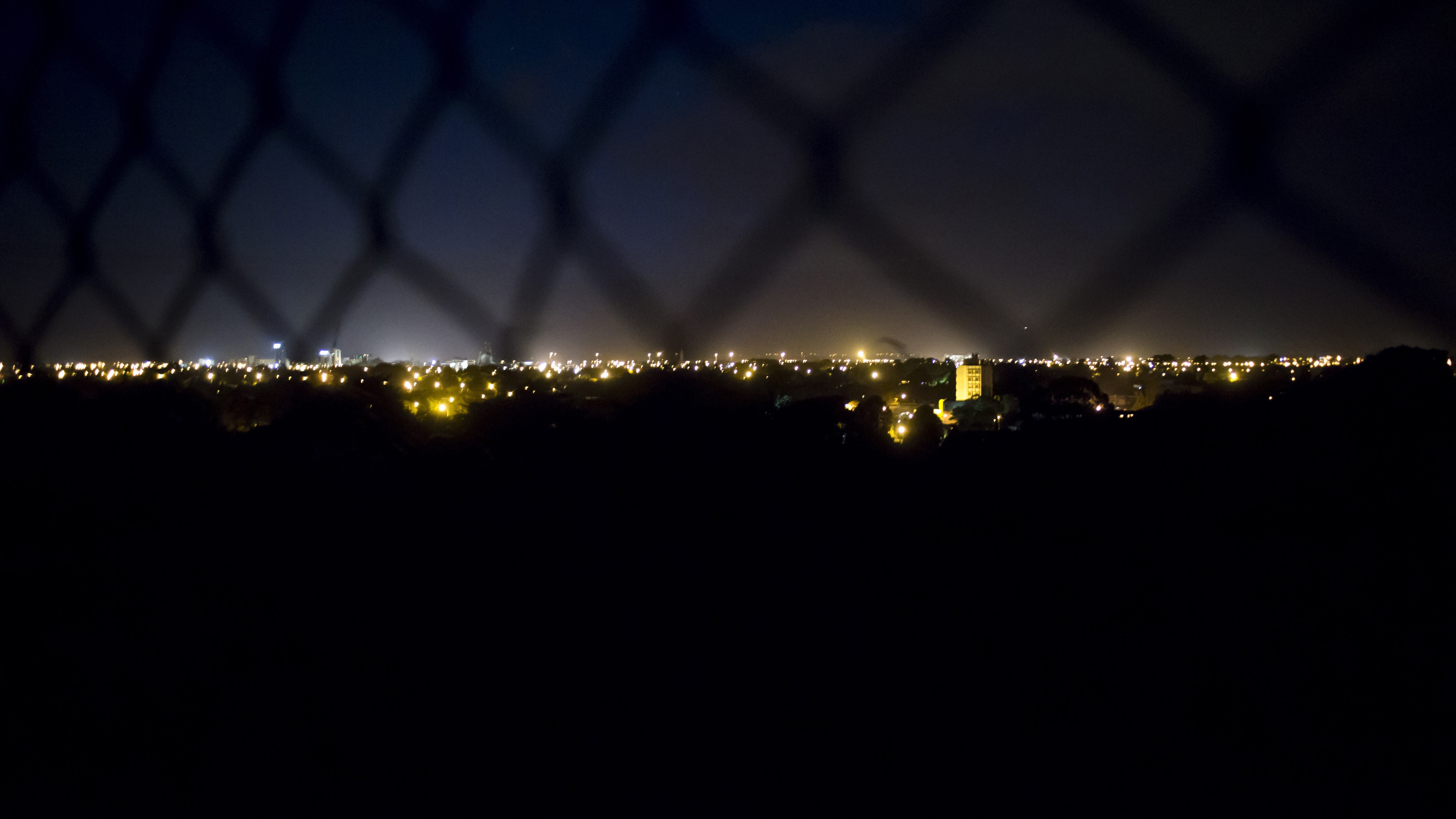 Cityscape at night seen through a fence HD Wallpaper