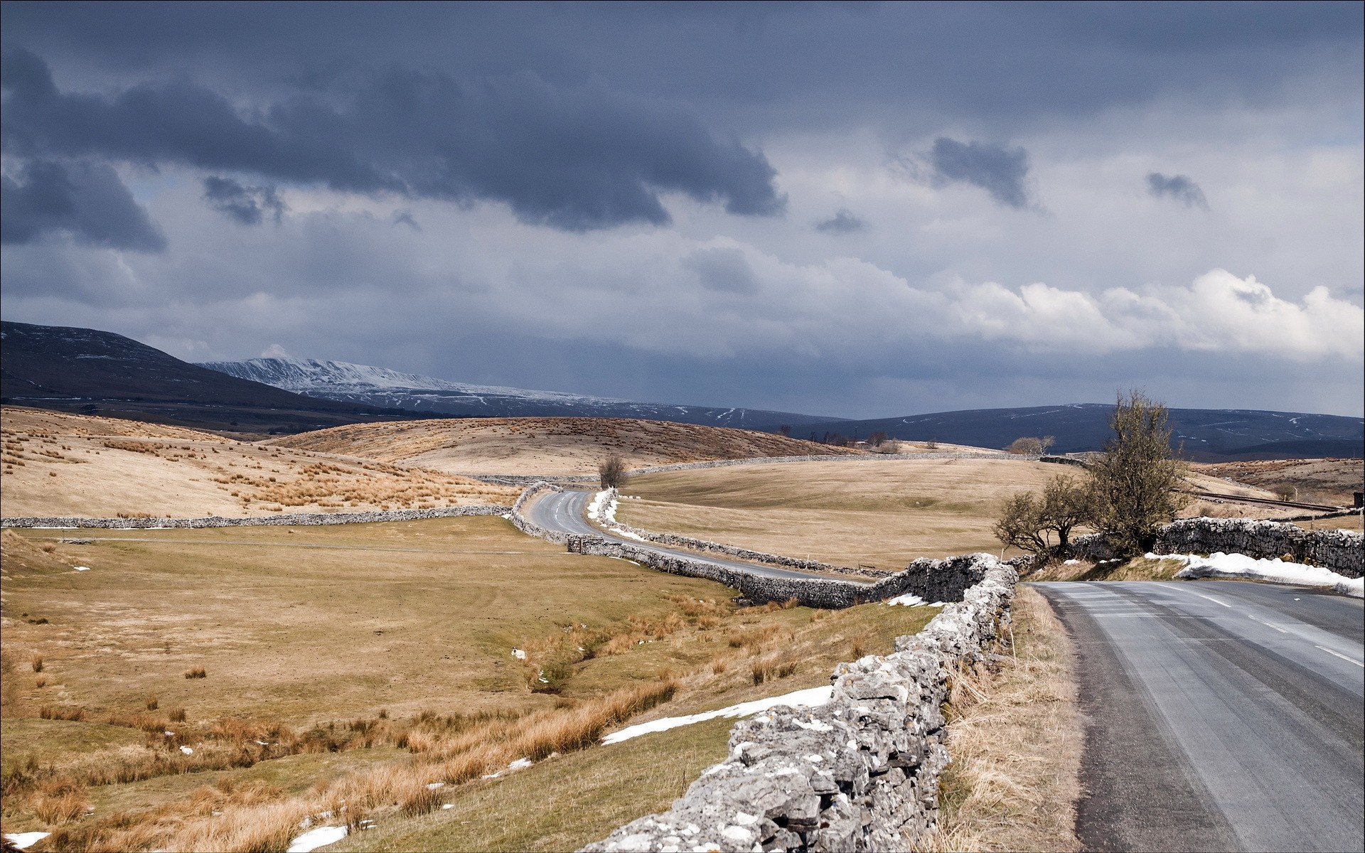 Winding road through a rural landscape with snow-capped mountains HD Wallpaper