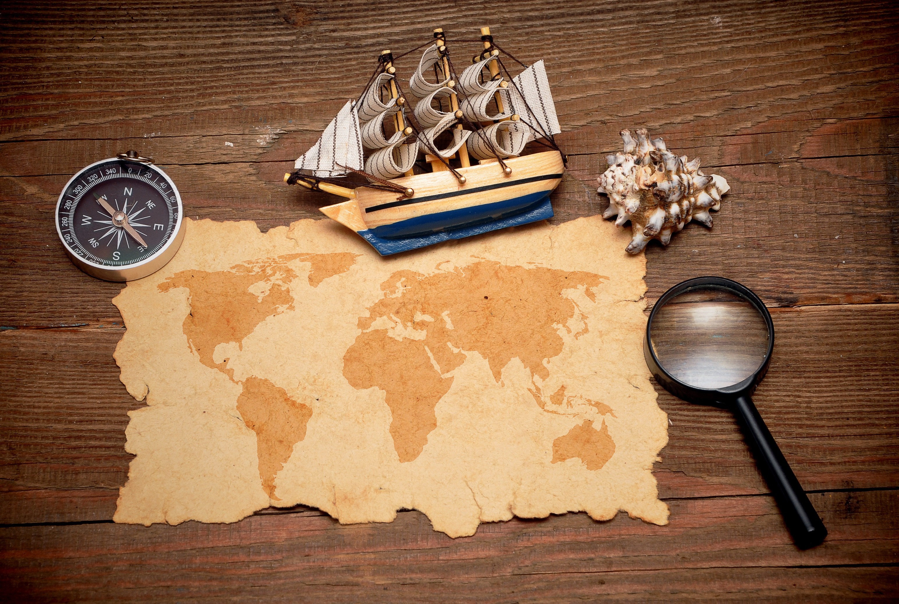 World map, compass, ship, seashell, and magnifying glass on wood HD Wallpaper