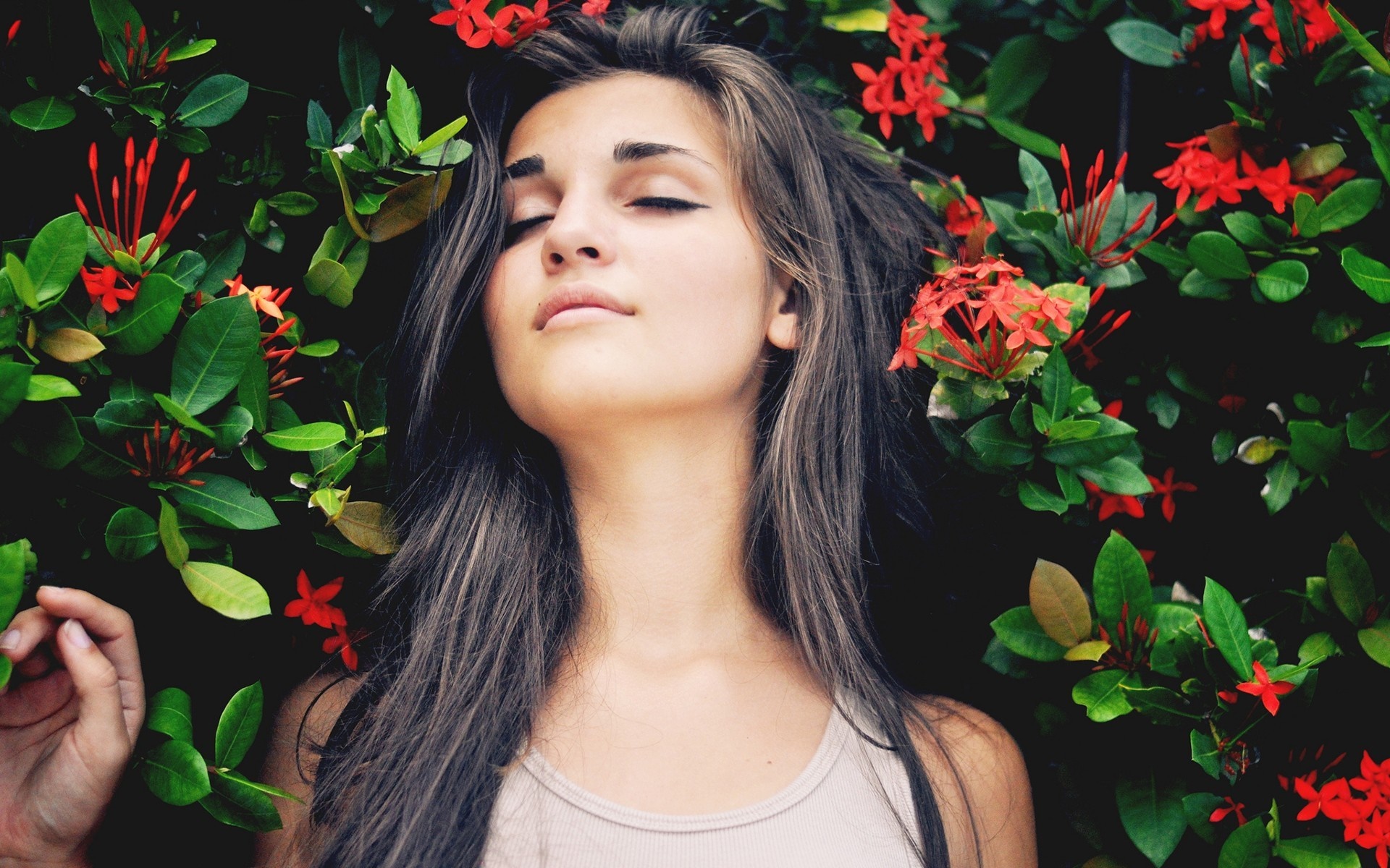 Woman with eyes closed surrounded by red flowers and green leaves HD Wallpaper