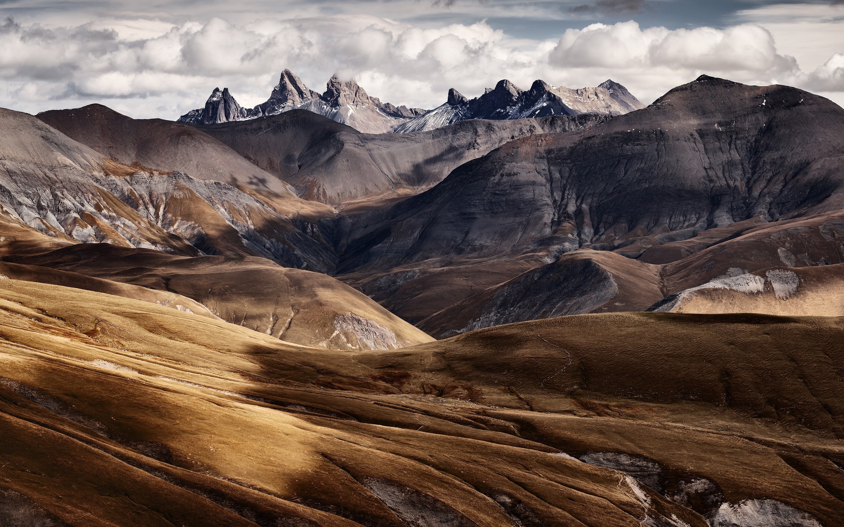 Mountain range with dramatic peaks and valleys under clouds HD Wallpaper