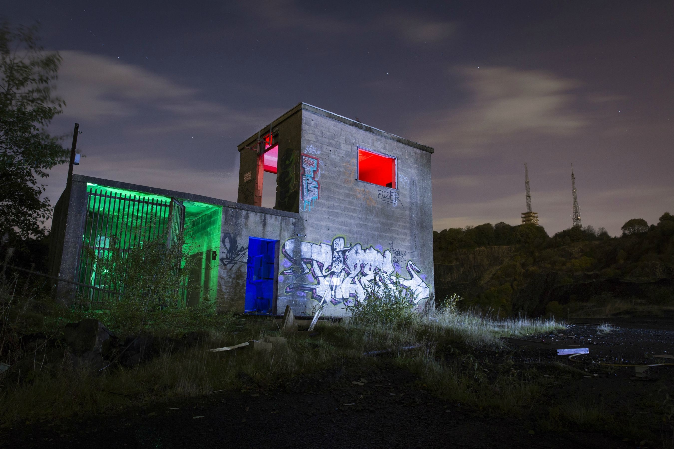 Graffiti-covered abandoned building at night with colored lights HD Wallpaper