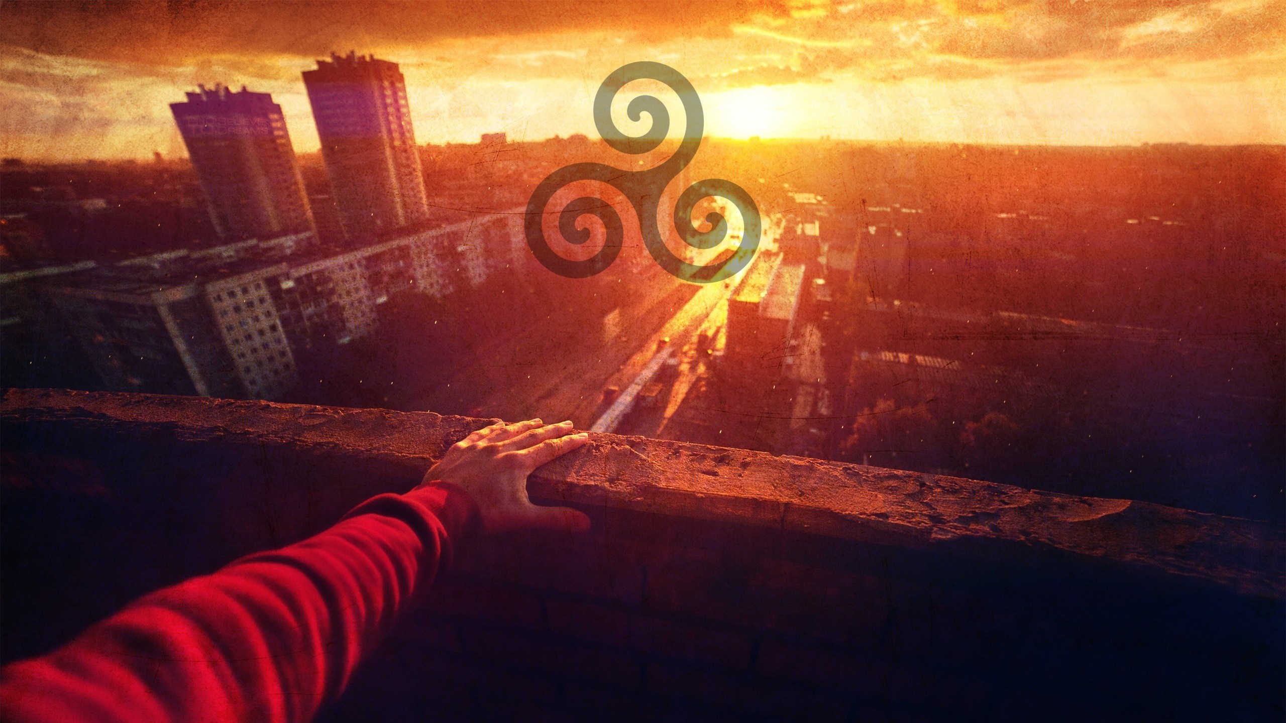 Hand on ledge overlooking city at sunset with triskel symbol HD Wallpaper