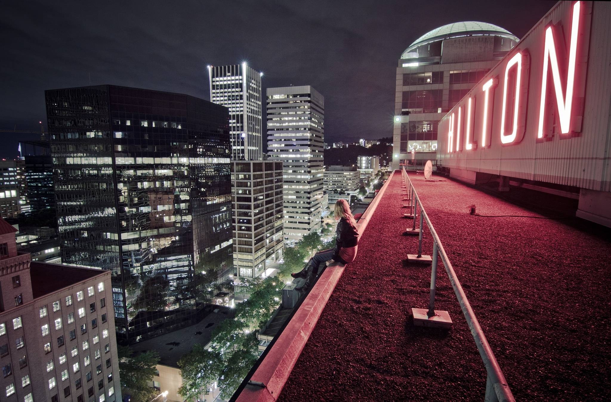 Woman sitting on a rooftop overlooking a city at night HD Wallpaper