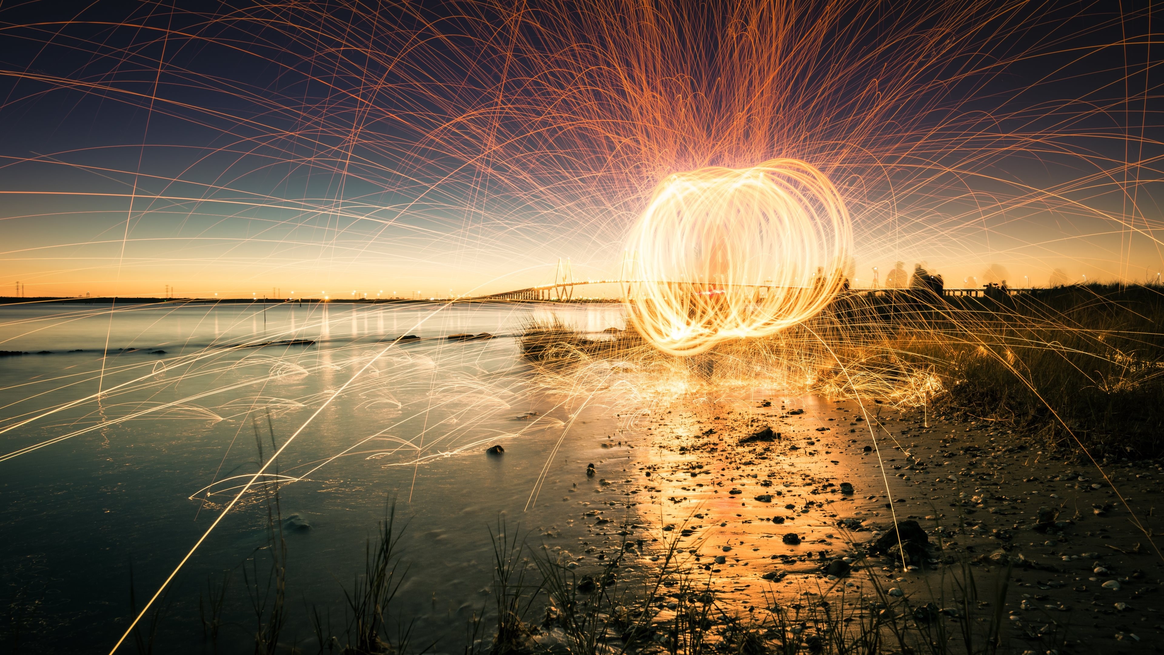 Steel wool spinning at sunset with bridge and water reflection HD Wallpaper