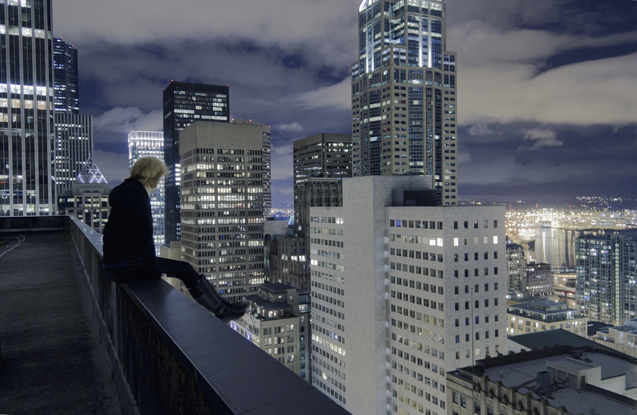 Woman sitting on a rooftop overlooking a city skyline at night HD Wallpaper