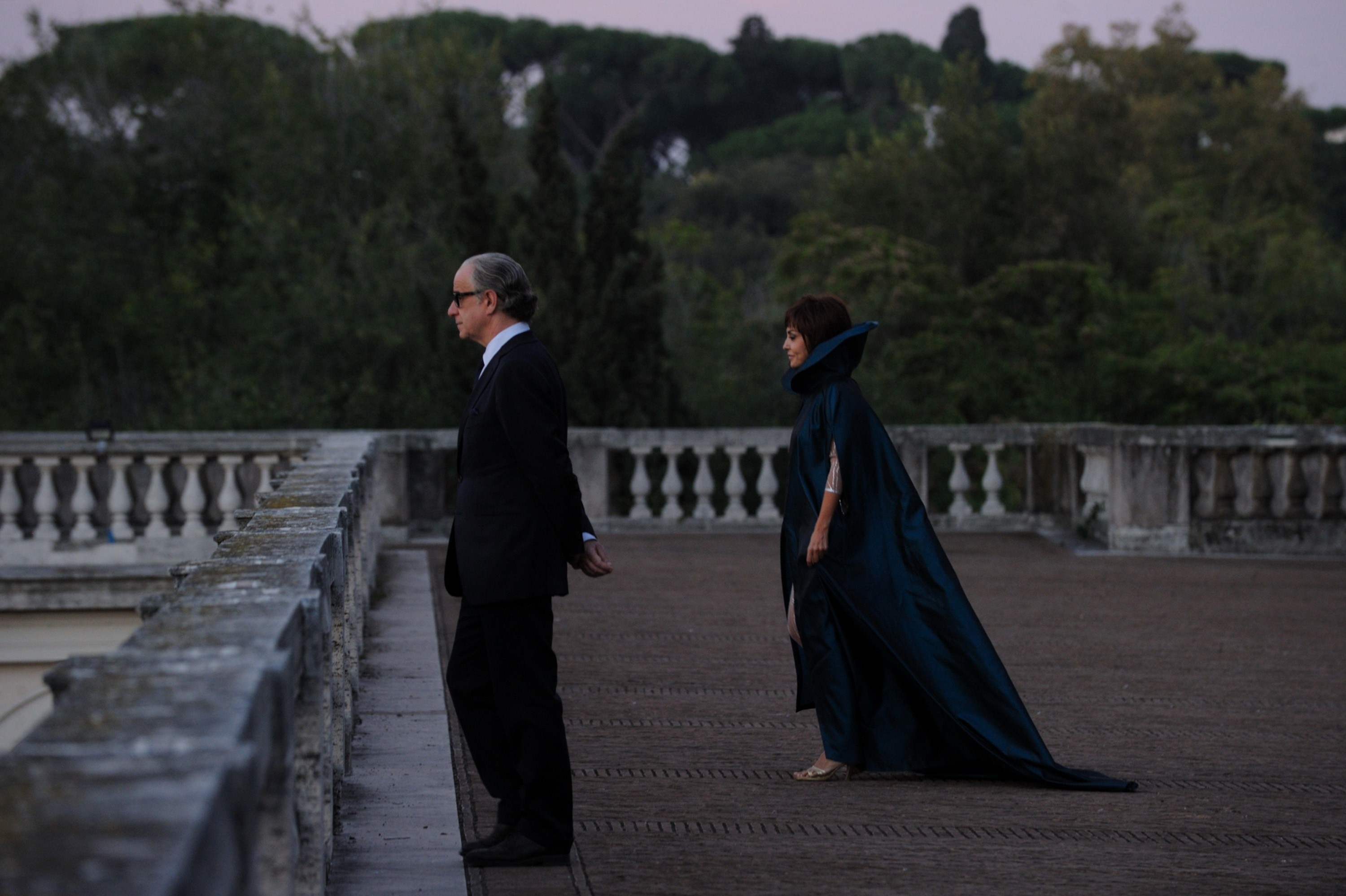 Man in suit and woman in cape on balcony HD Wallpaper