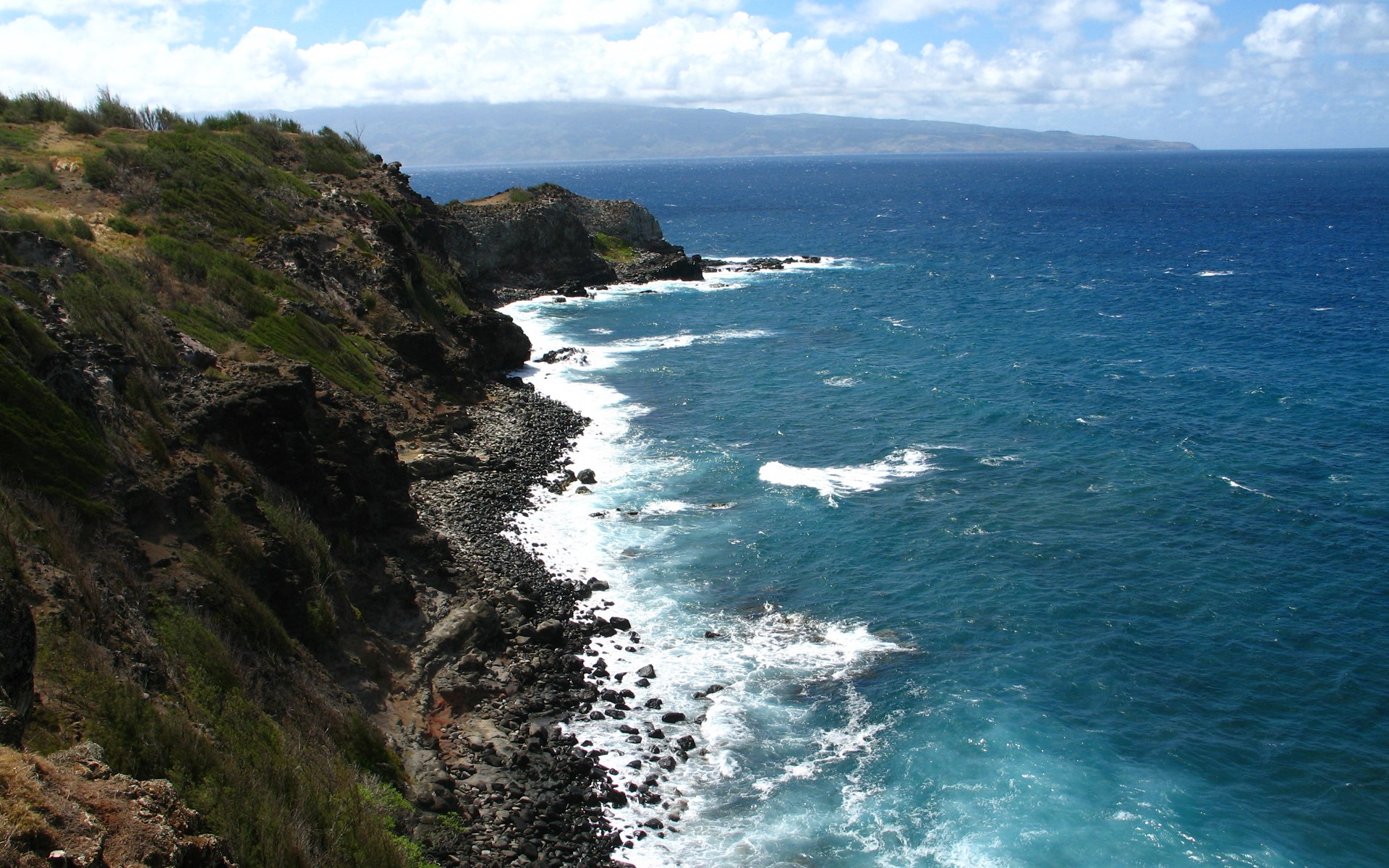Rocky coastline with blue ocean and distant mountains HD Wallpaper