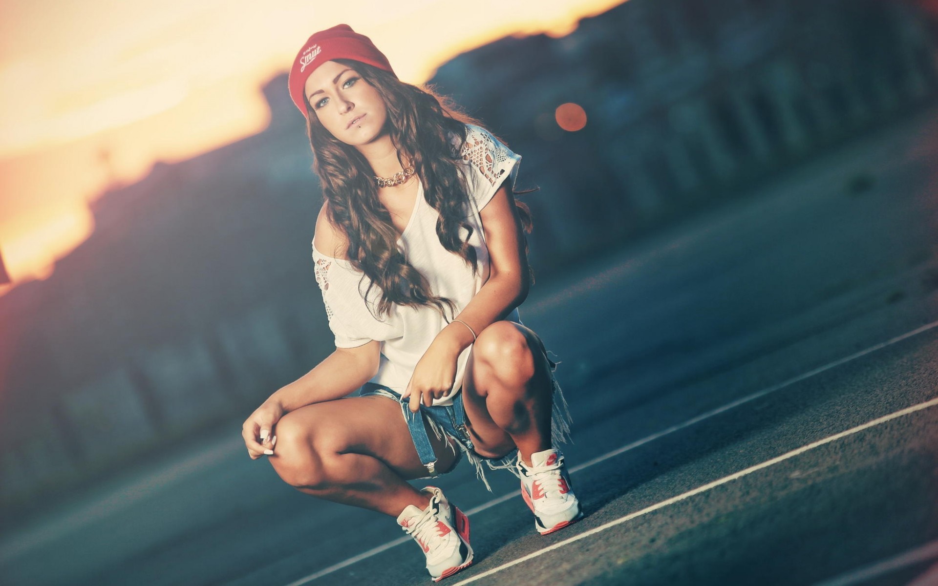 Woman in red beanie and denim shorts crouching outdoors HD Wallpaper