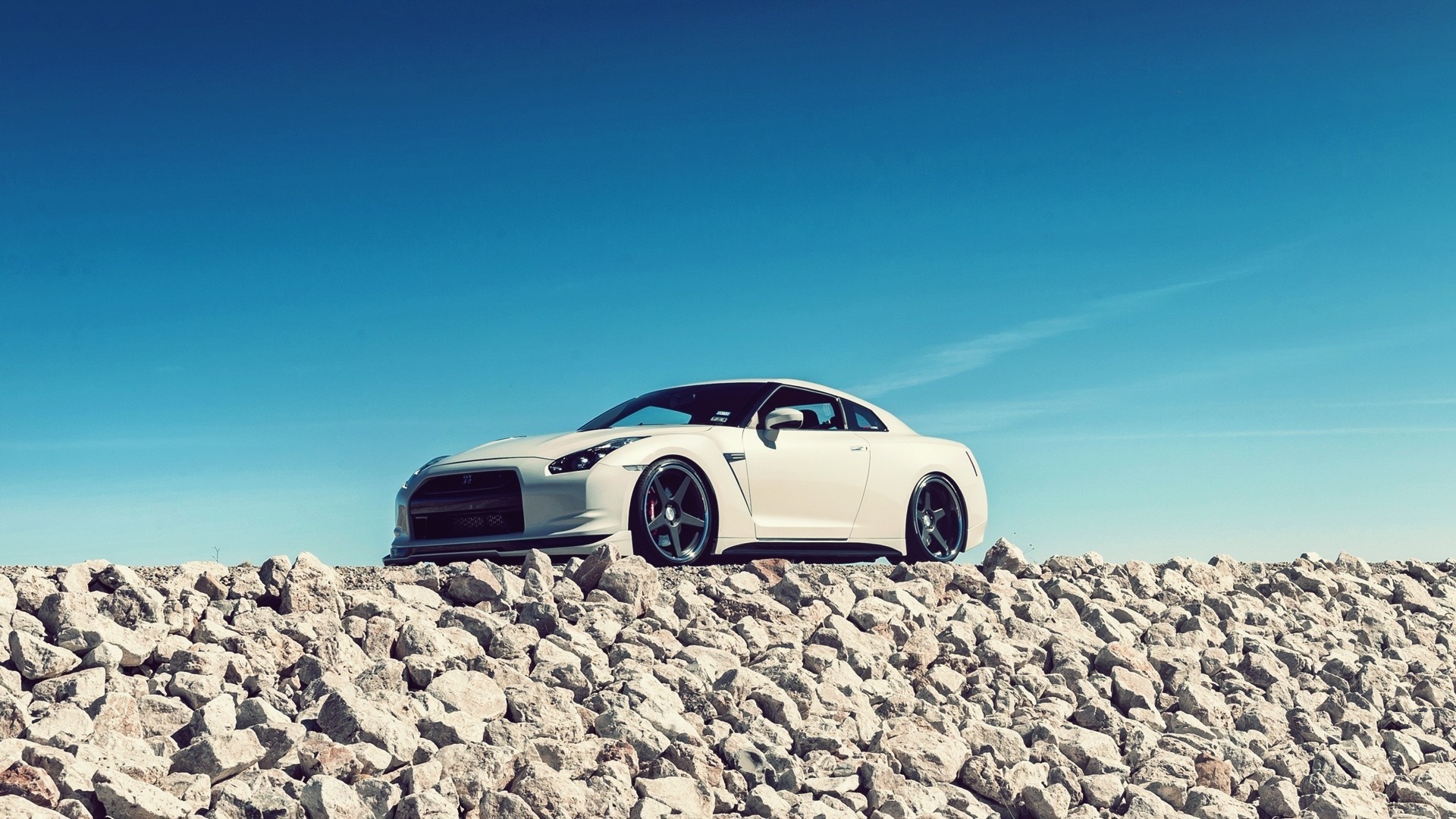 White Nissan GT-R on a rocky embankment under a blue sky HD Wallpaper
