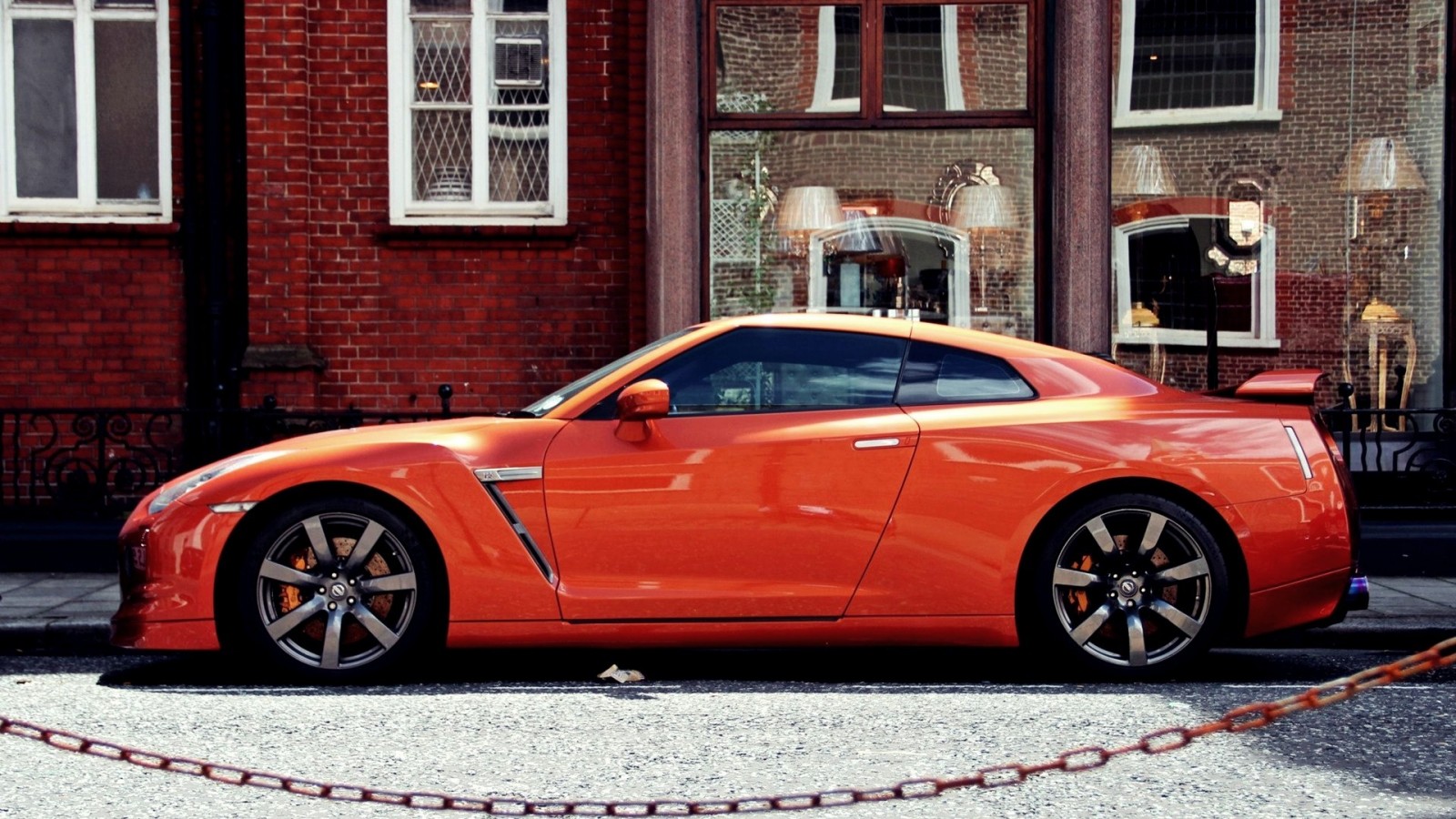 Orange Nissan GT-R parked in front of a brick building HD Wallpaper