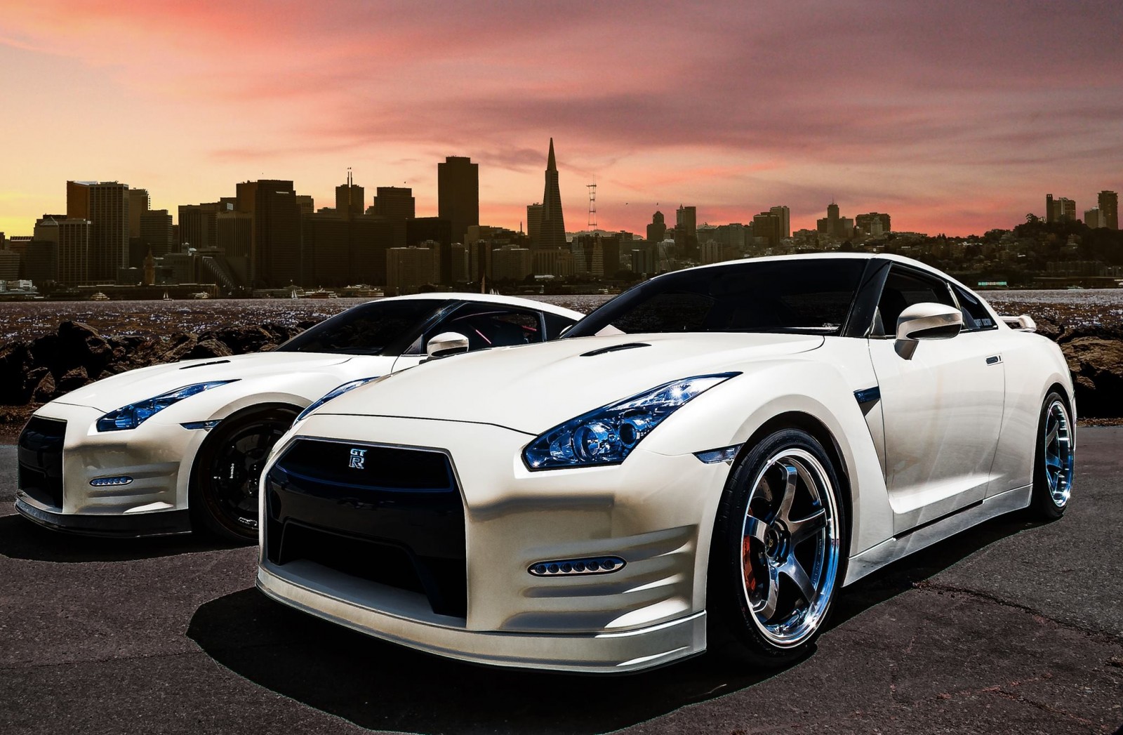 Two white Nissan GT-R sports cars with city skyline at sunset HD Wallpaper