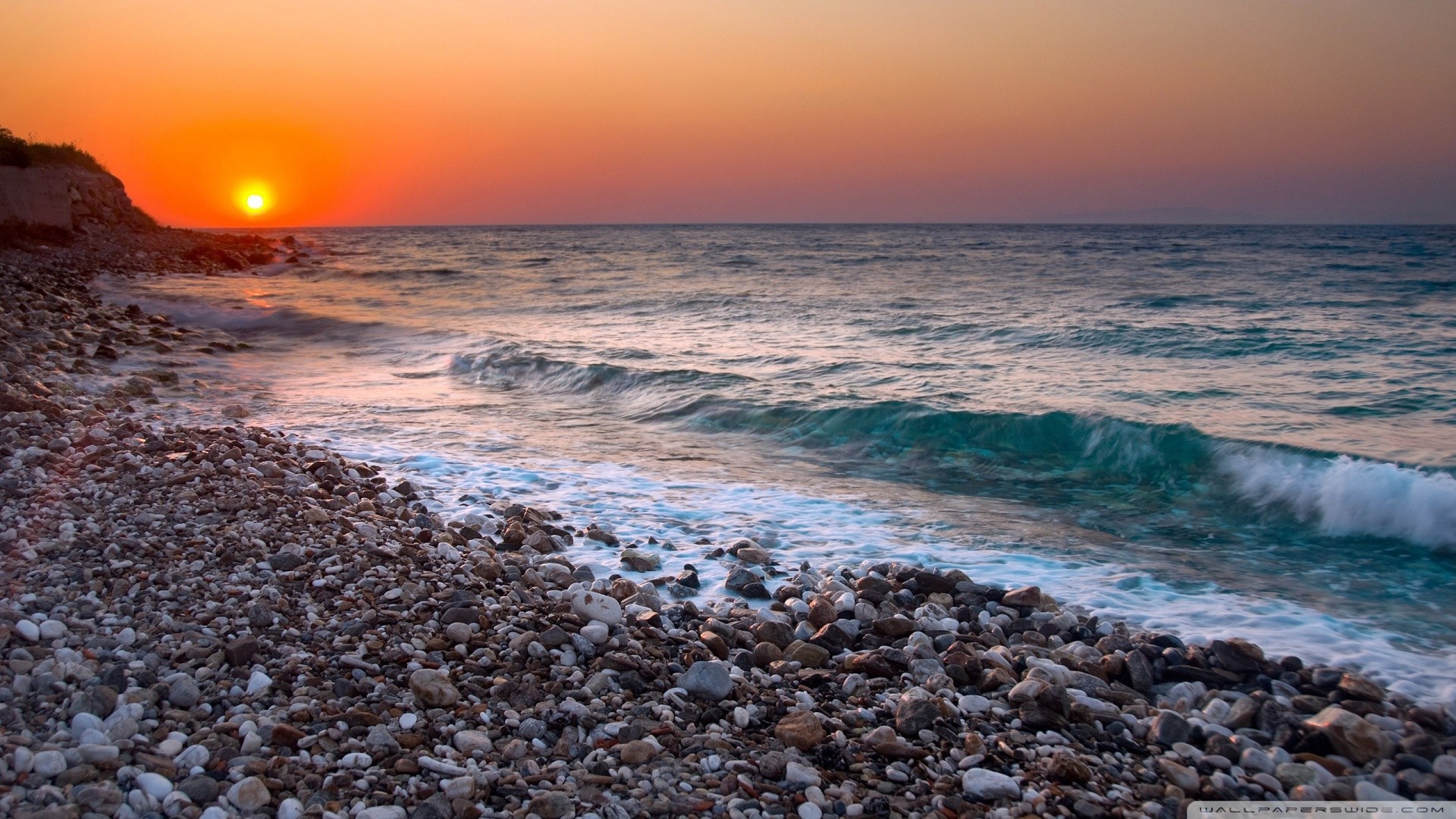 Sunset over a rocky beach with waves HD Wallpaper