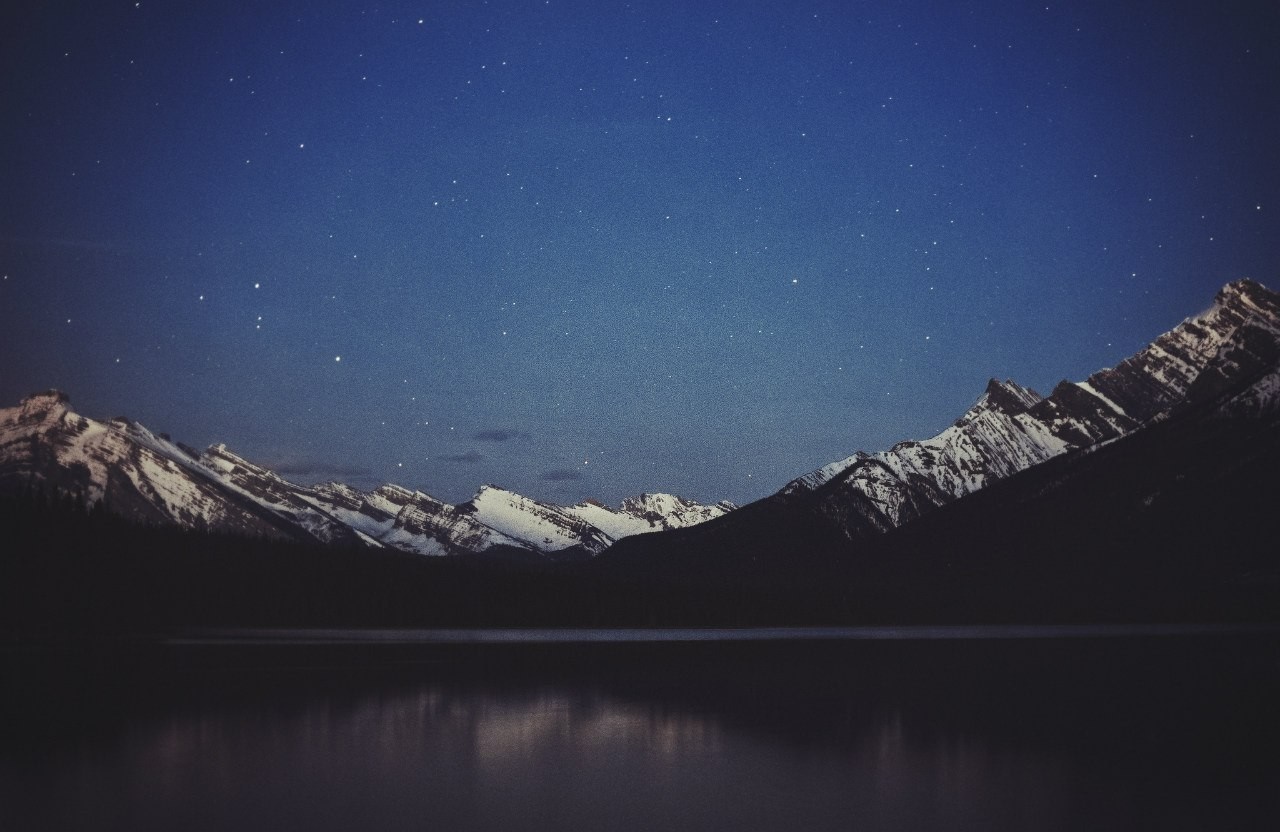 Snowy mountains reflected in a lake under a starry night sky HD Wallpaper