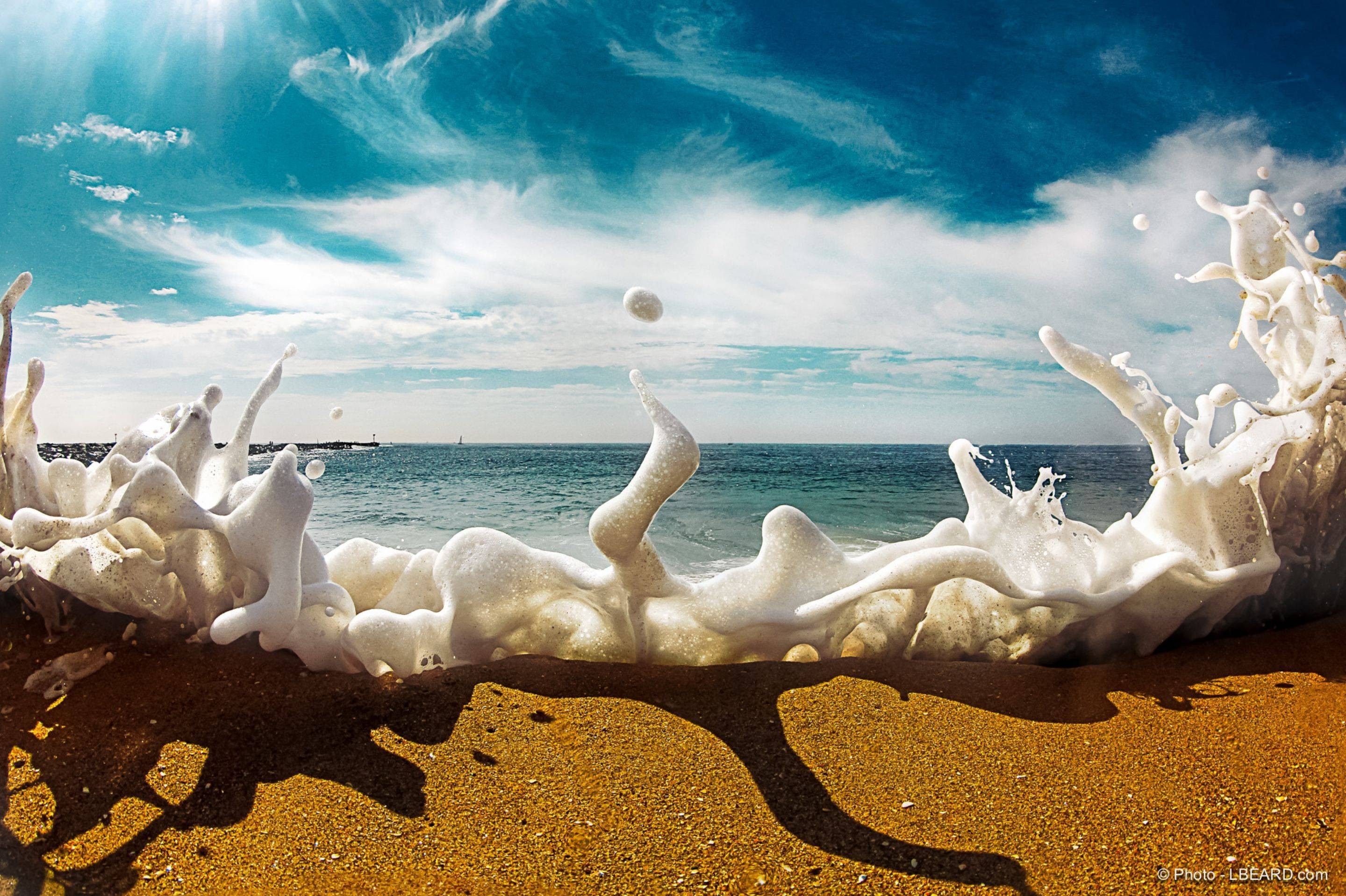 Wave crashing on a sandy beach with blue sky and clouds HD Wallpaper