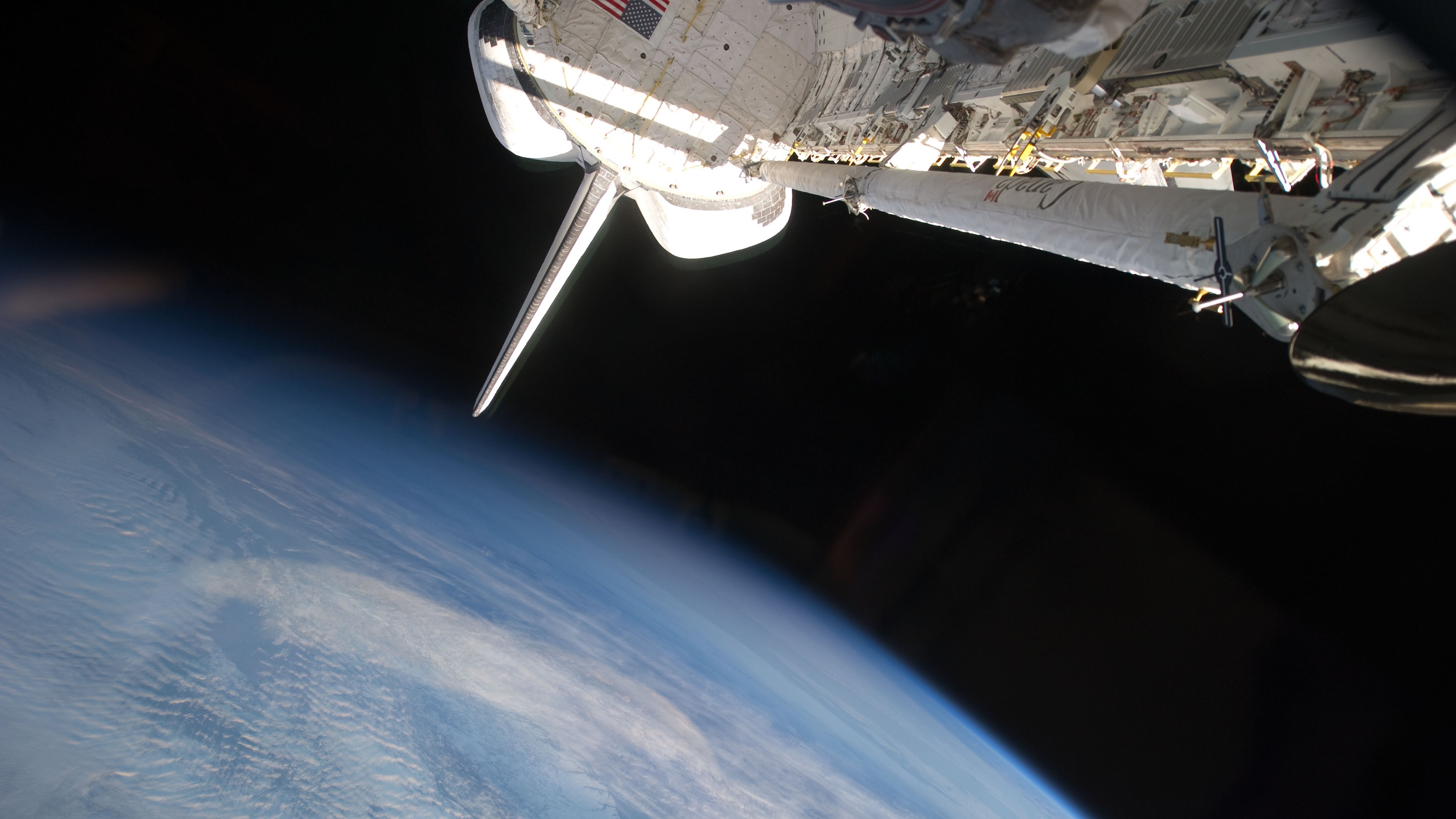 Space Shuttle orbiting Earth with sunlight reflection HD Wallpaper