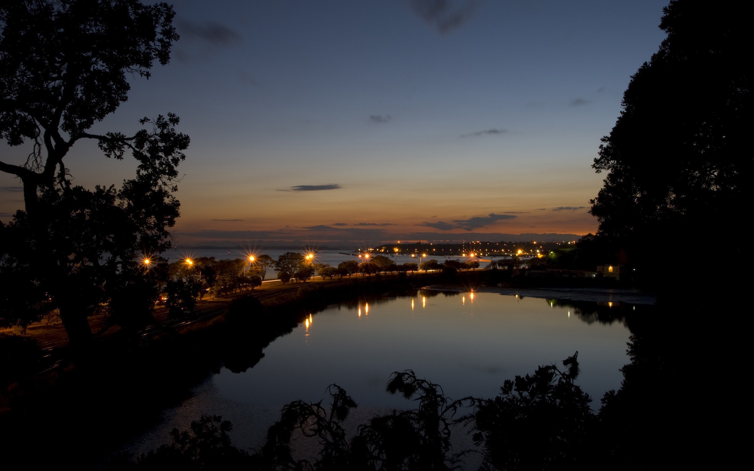 Cityscape at dusk with lake reflection and trees HD Wallpaper