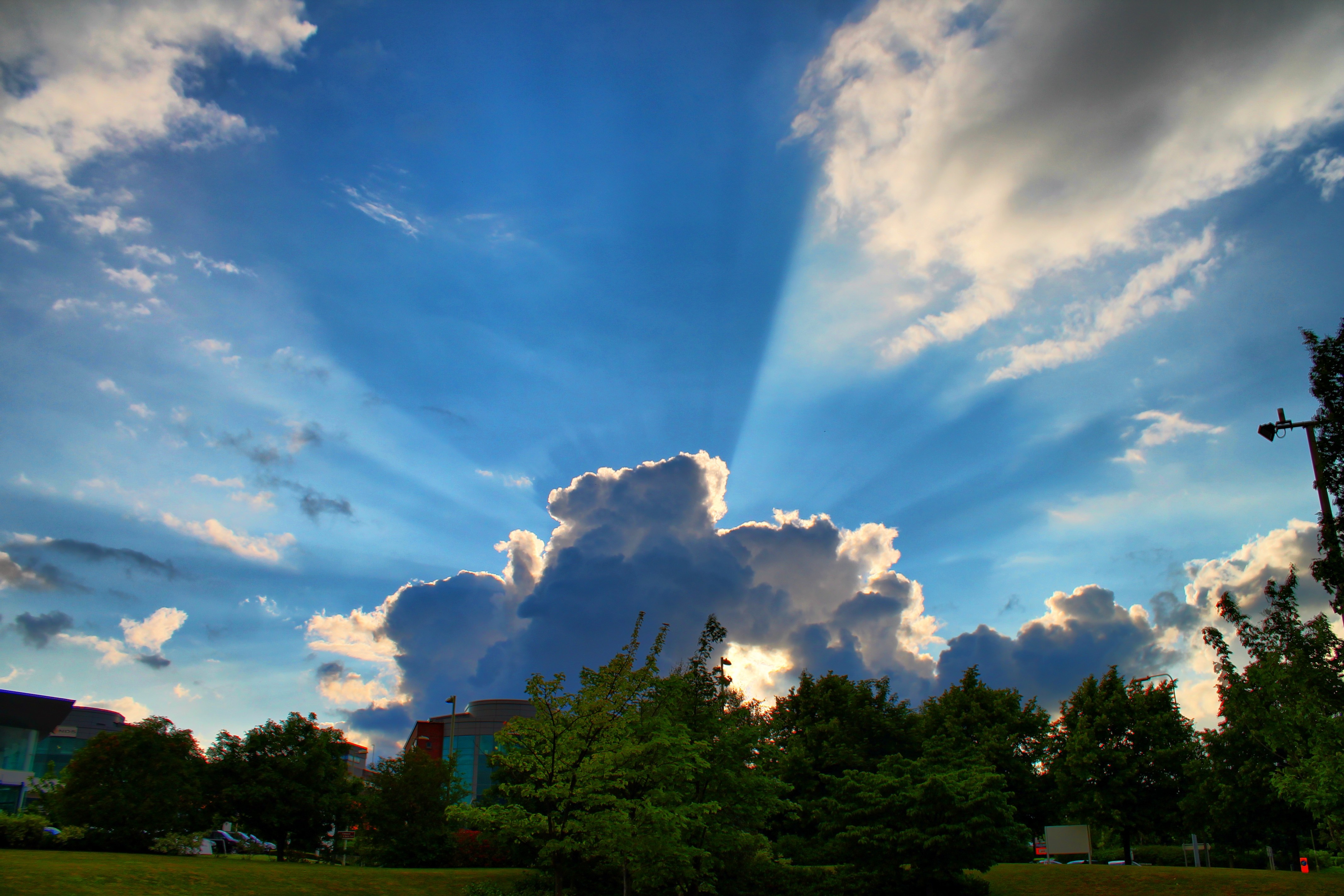 Sunbeams through clouds over trees and buildings HD Wallpaper