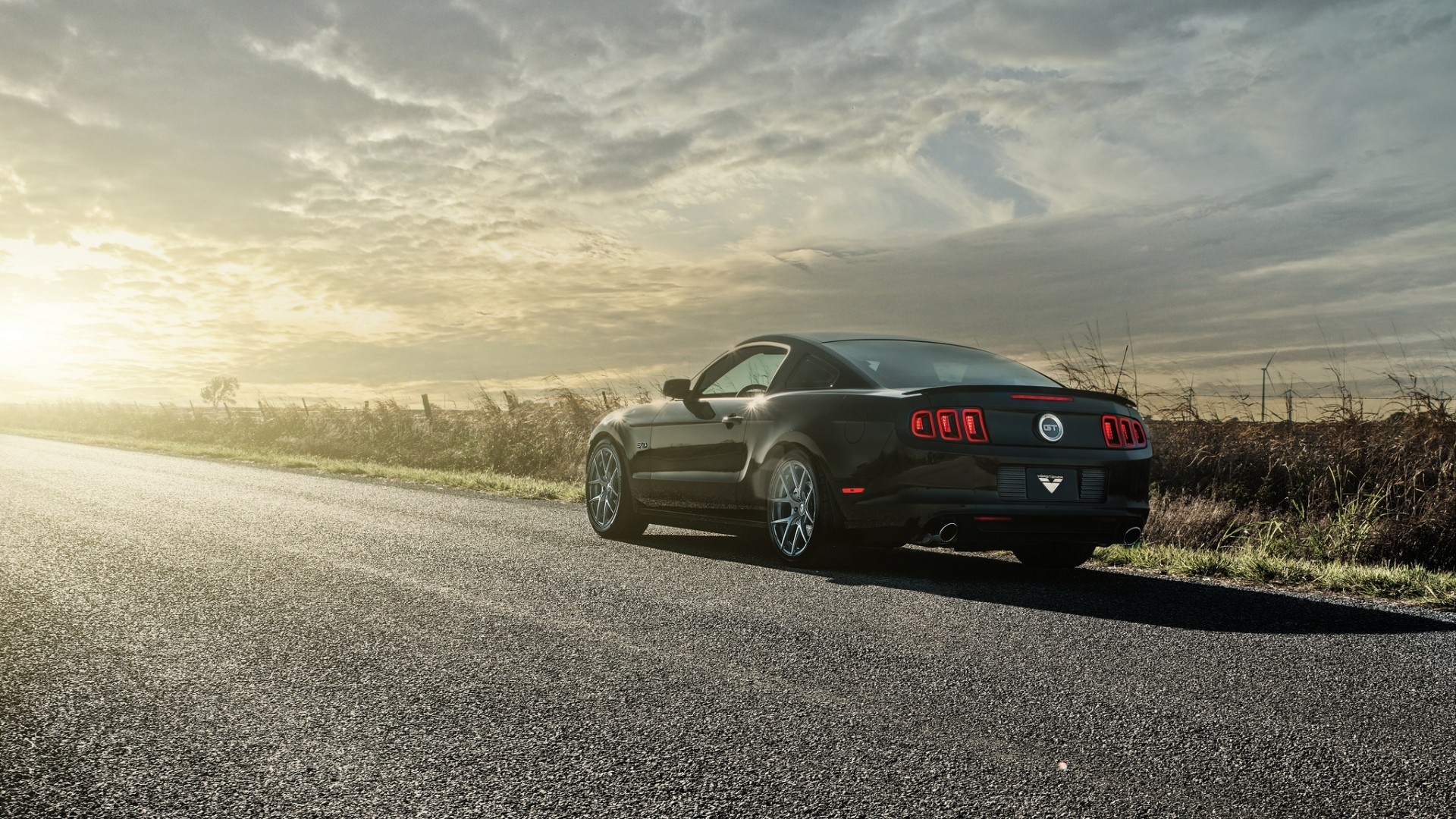 Black Ford Mustang GT driving on a road at sunset HD Wallpaper