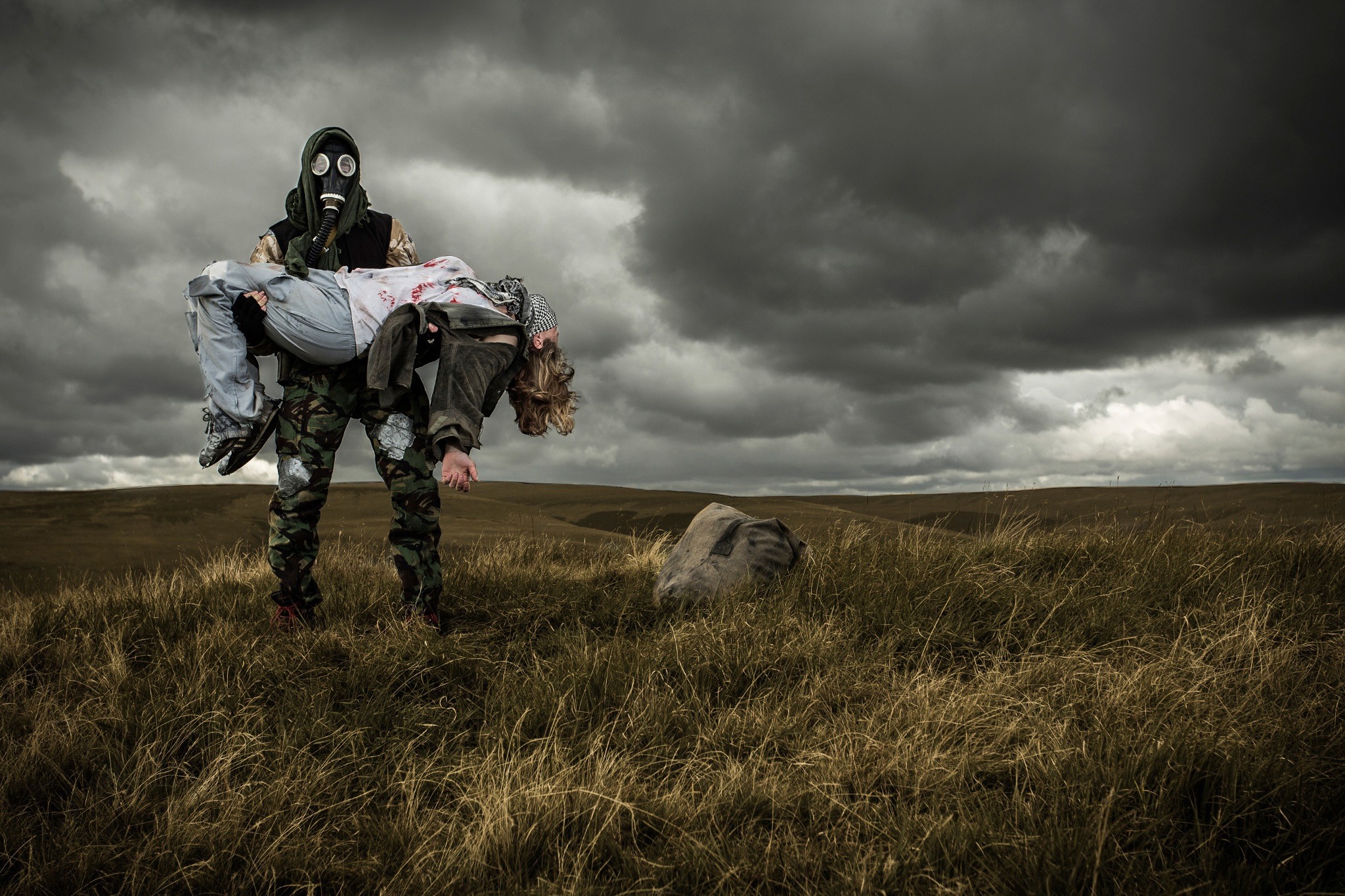 Man in gas mask carrying injured person in field HD Wallpaper