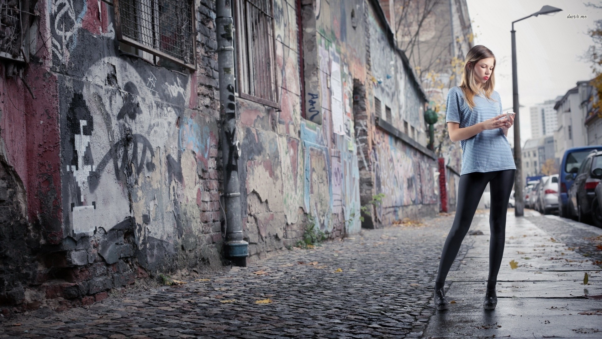 Woman looking at phone on graffiti-covered street HD Wallpaper