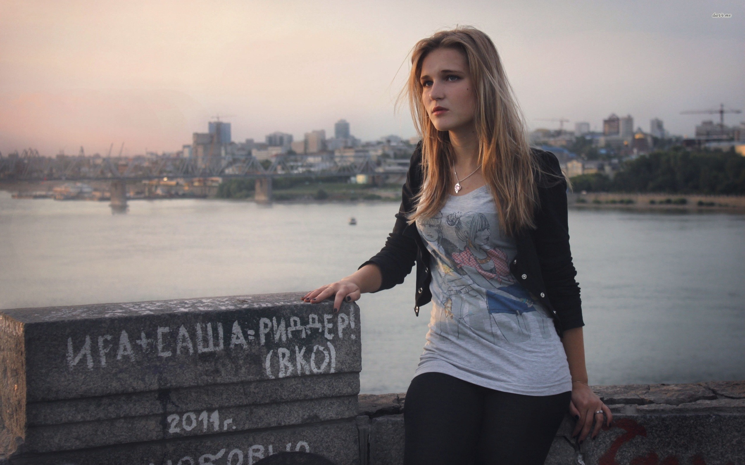 Young woman posing on a bridge overlooking a city at sunset HD Wallpaper