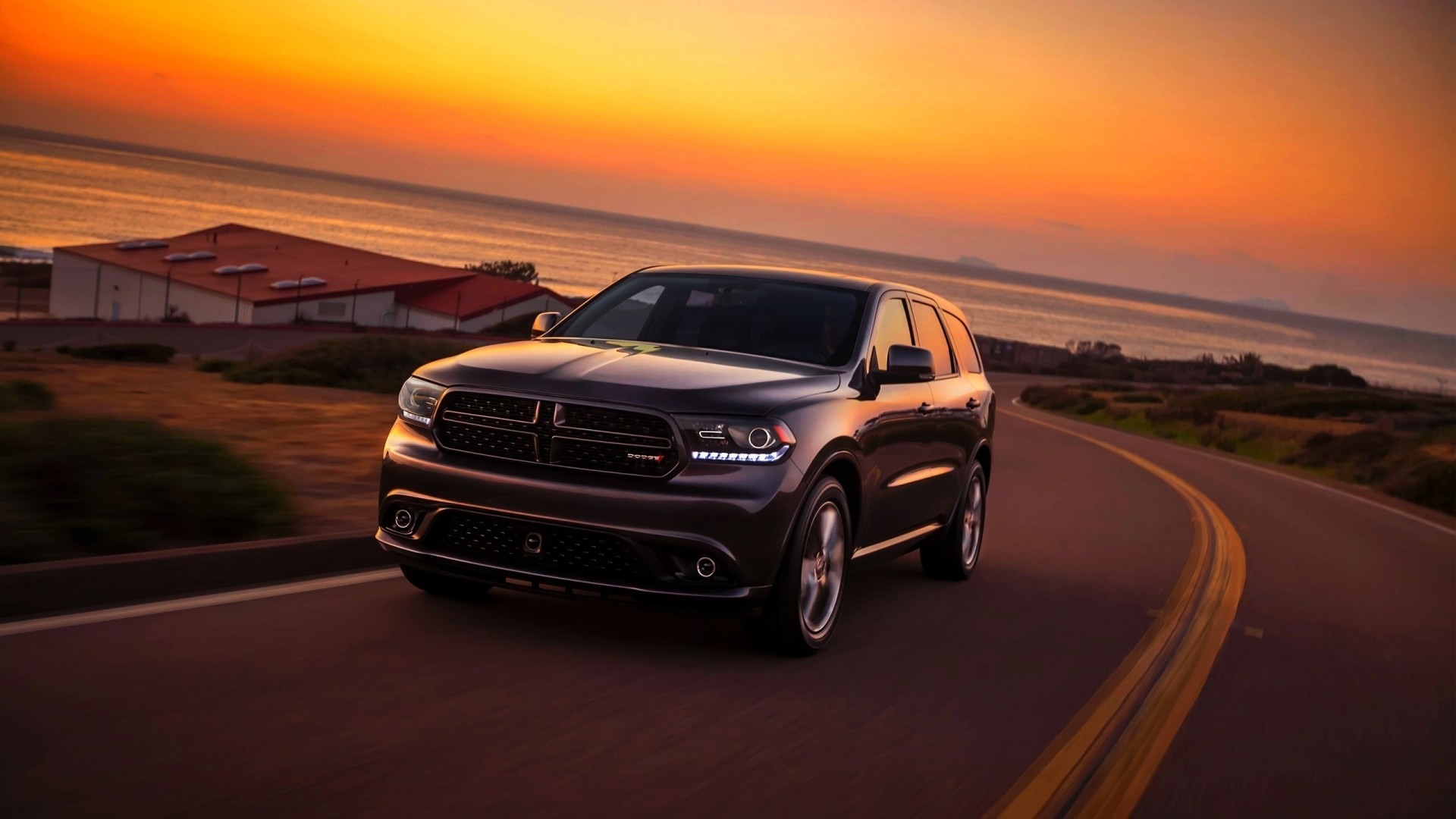 Dodge Durango driving on a coastal road at sunset HD Wallpaper