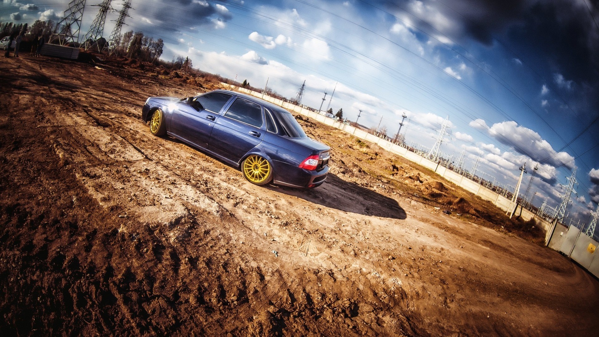 Blue sedan with gold rims on a dirt road HD Wallpaper