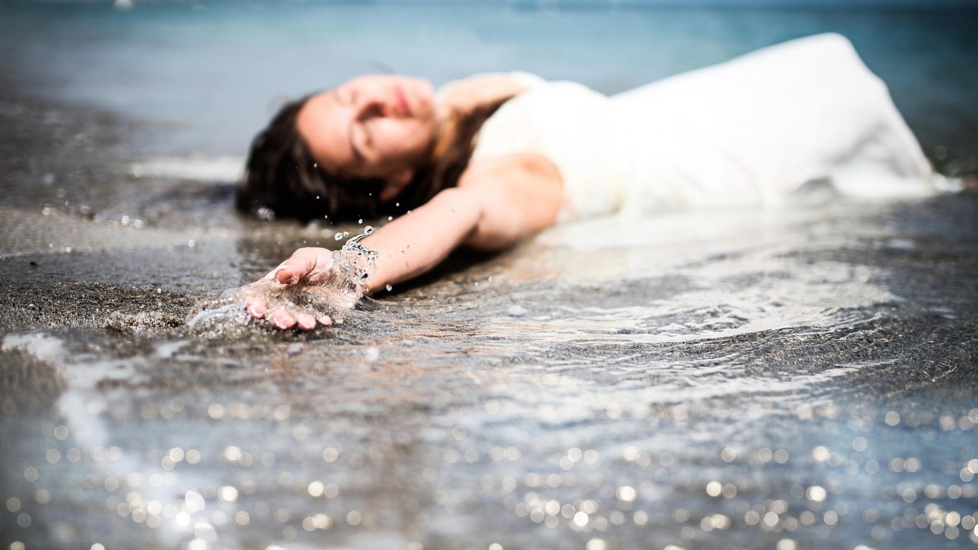 Woman lying on a beach with water on her hand HD Wallpaper