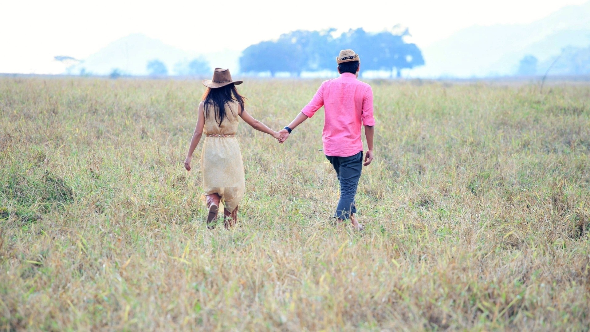 Couple holding hands walking in a grassy field HD Wallpaper