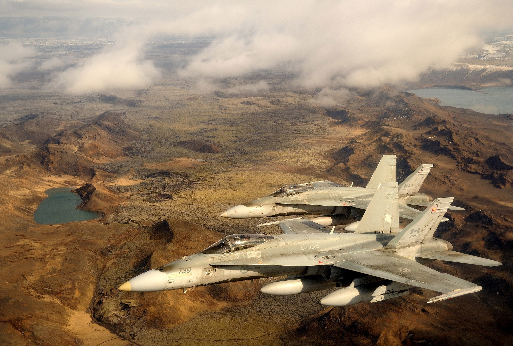 Two Canadian CF-18 Hornets fly over a rugged landscape HD Wallpaper