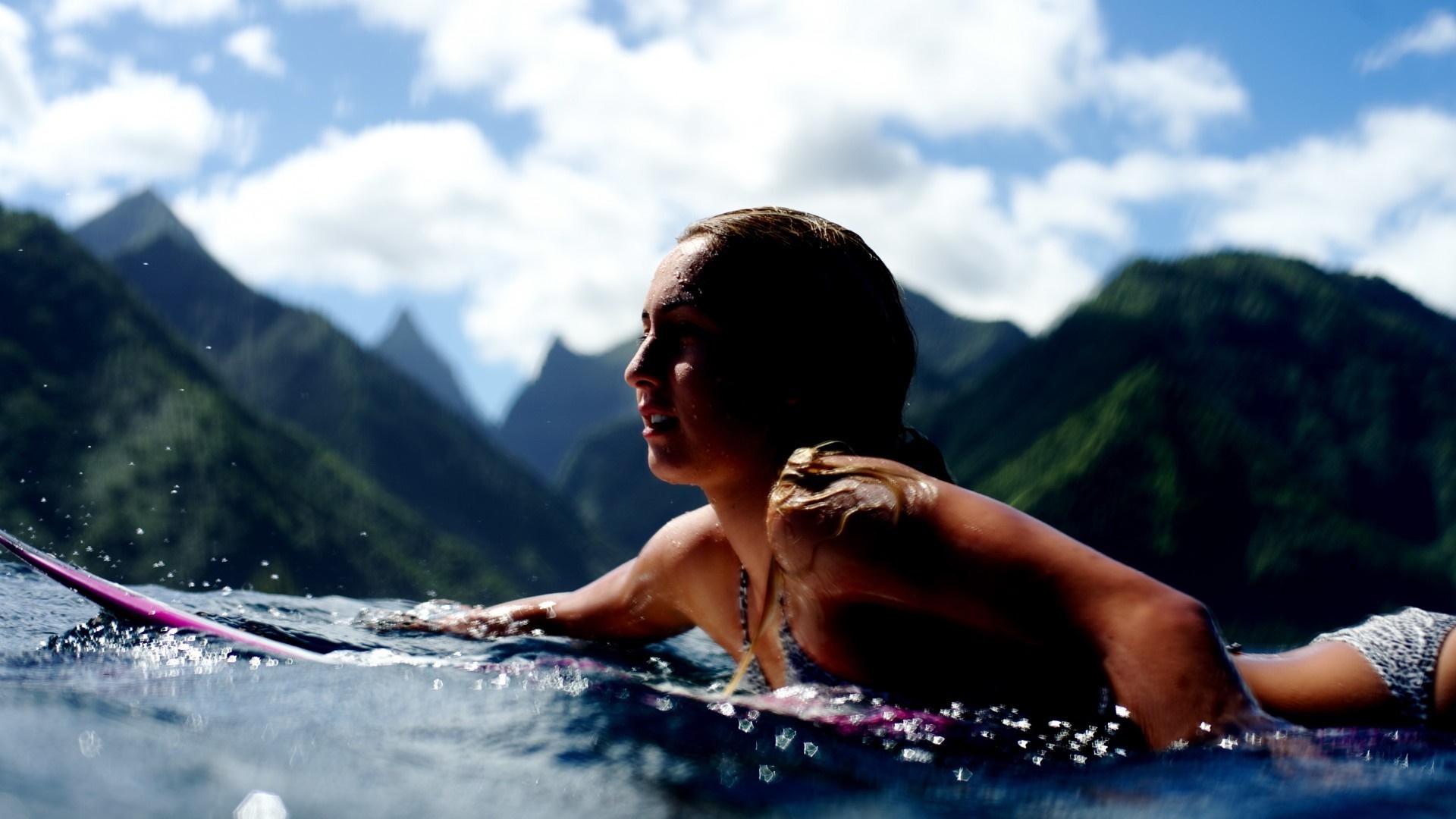 Woman surfing in the ocean with mountains in the background HD Wallpaper