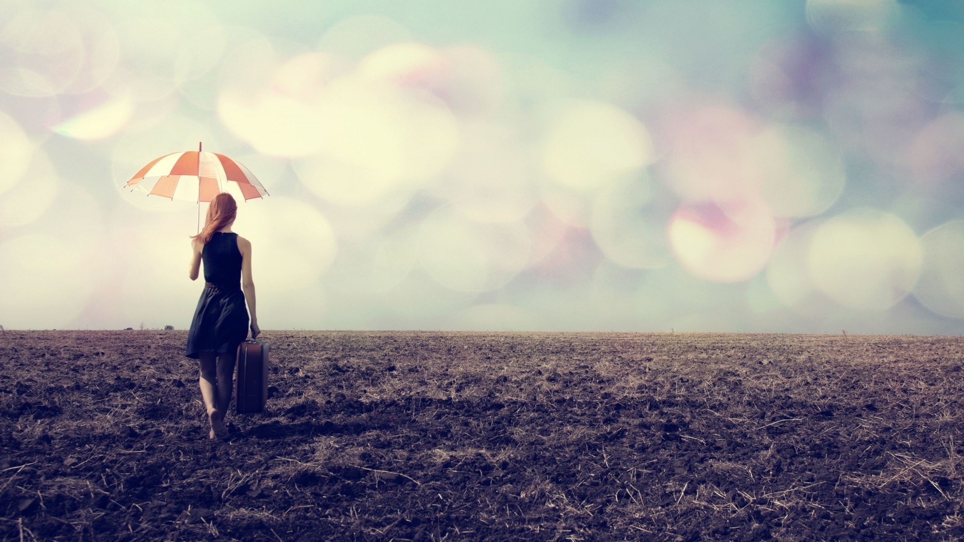Woman with umbrella and suitcase in a field HD Wallpaper