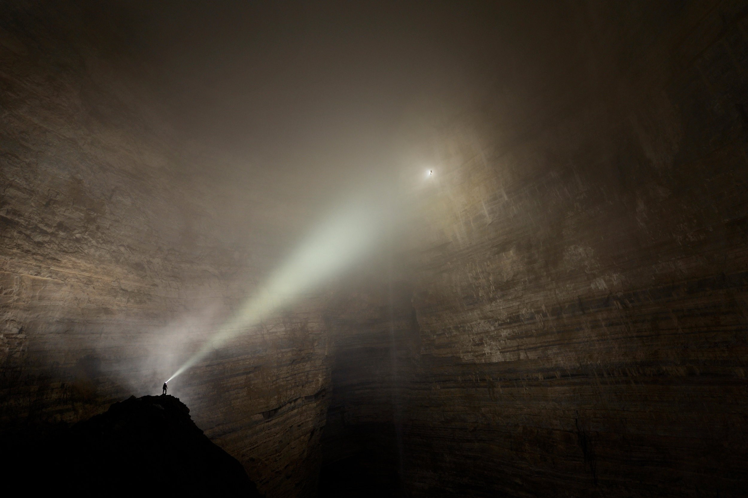 Person with flashlight in a vast cave with fog HD Wallpaper