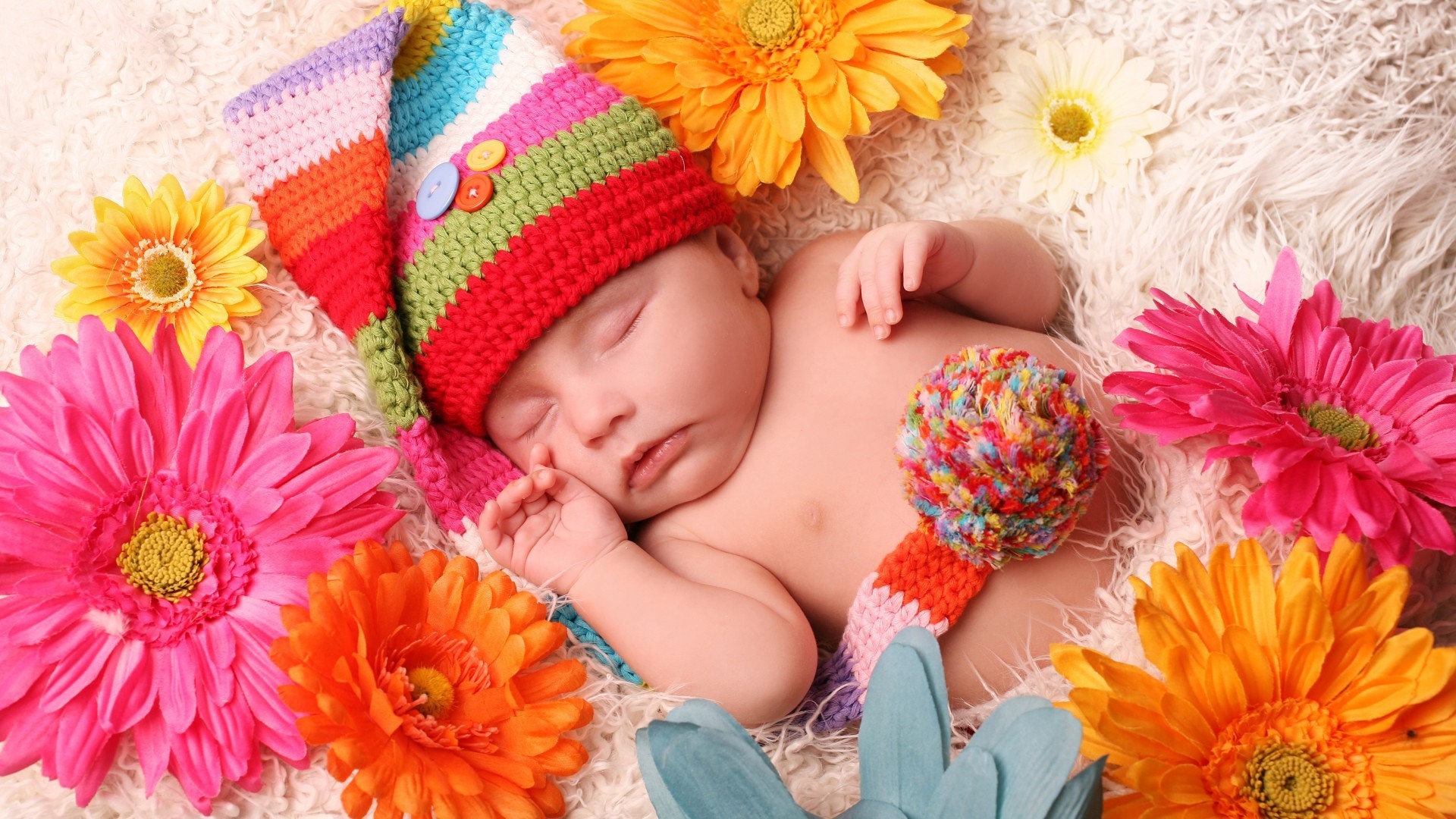 Baby in colorful hat surrounded by flowers HD Wallpaper