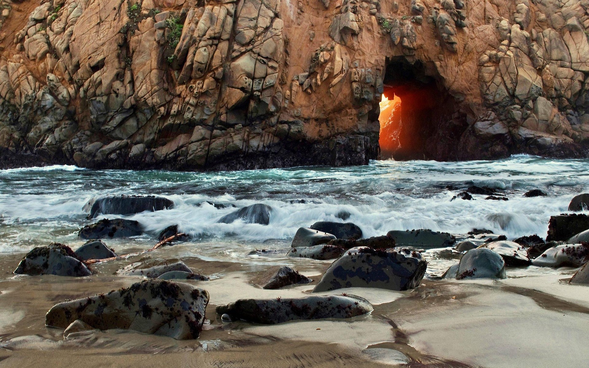 Cave entrance in a rocky coast with waves crashing HD Wallpaper