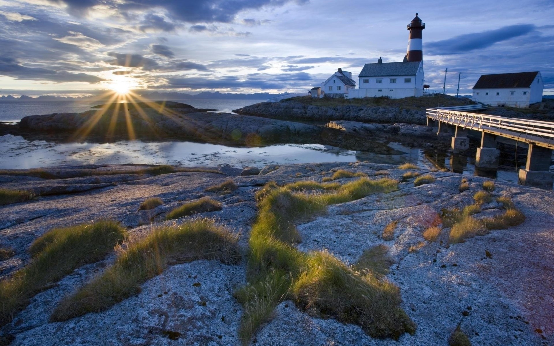 Lighthouse and buildings on a rocky coast at sunset HD Wallpaper