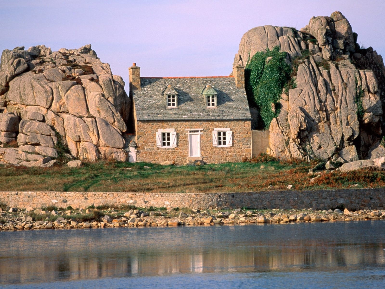 Stone house nestled between large rocks by the water HD Wallpaper