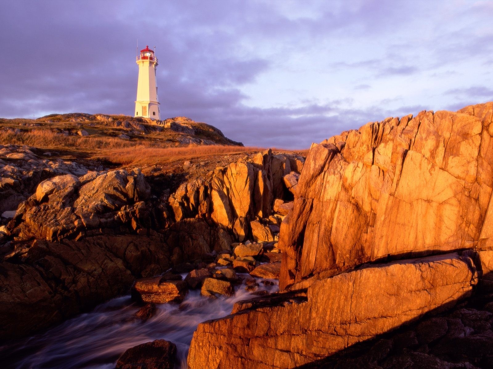 Lighthouse on a rocky coast at sunset HD Wallpaper
