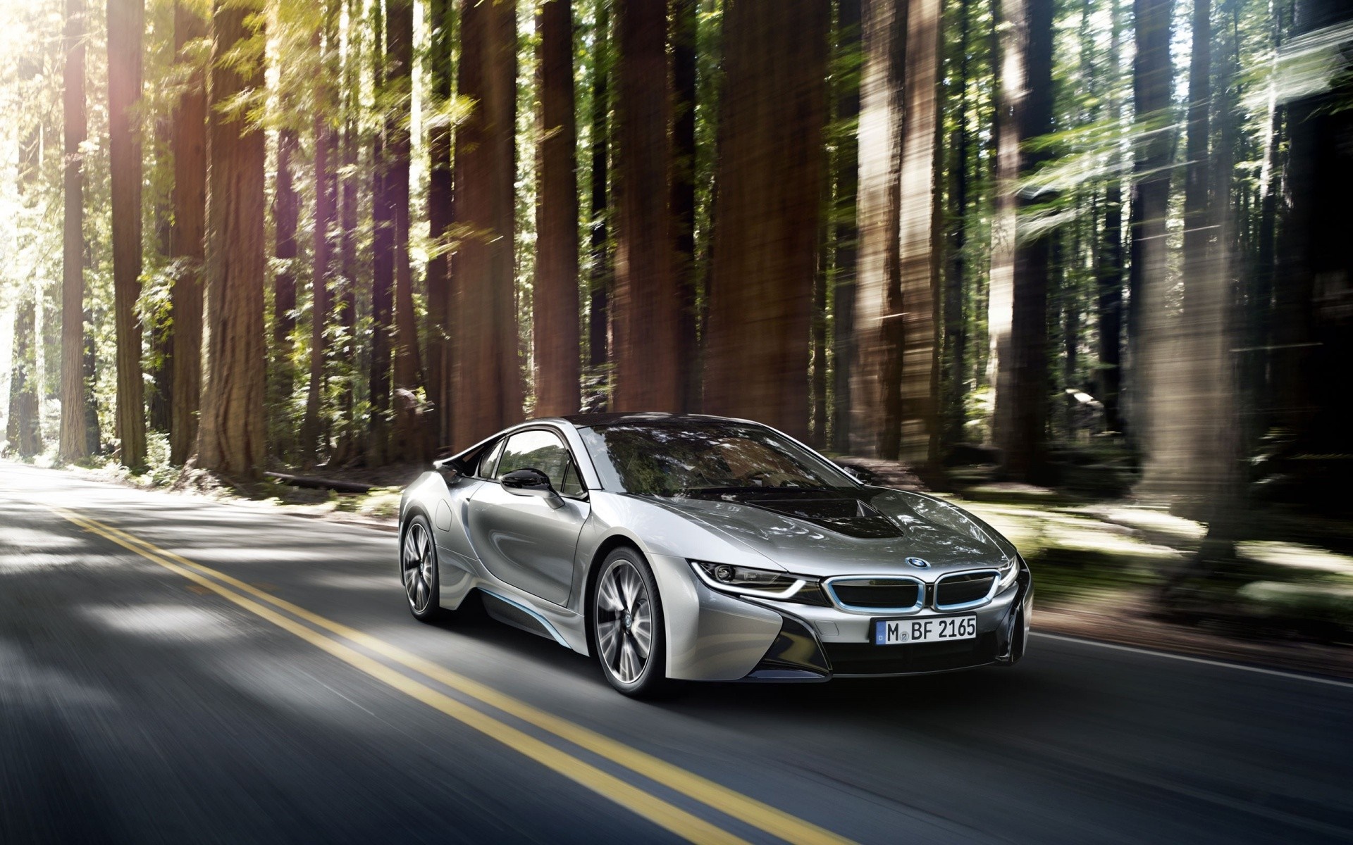 Silver BMW i8 driving on a road through a forest HD Wallpaper