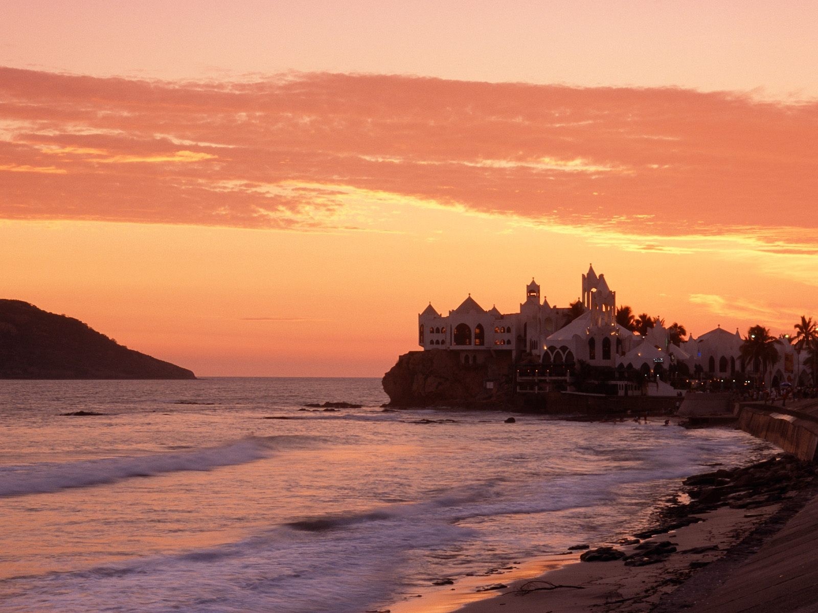 White building on a cliff overlooking the ocean at sunset HD Wallpaper